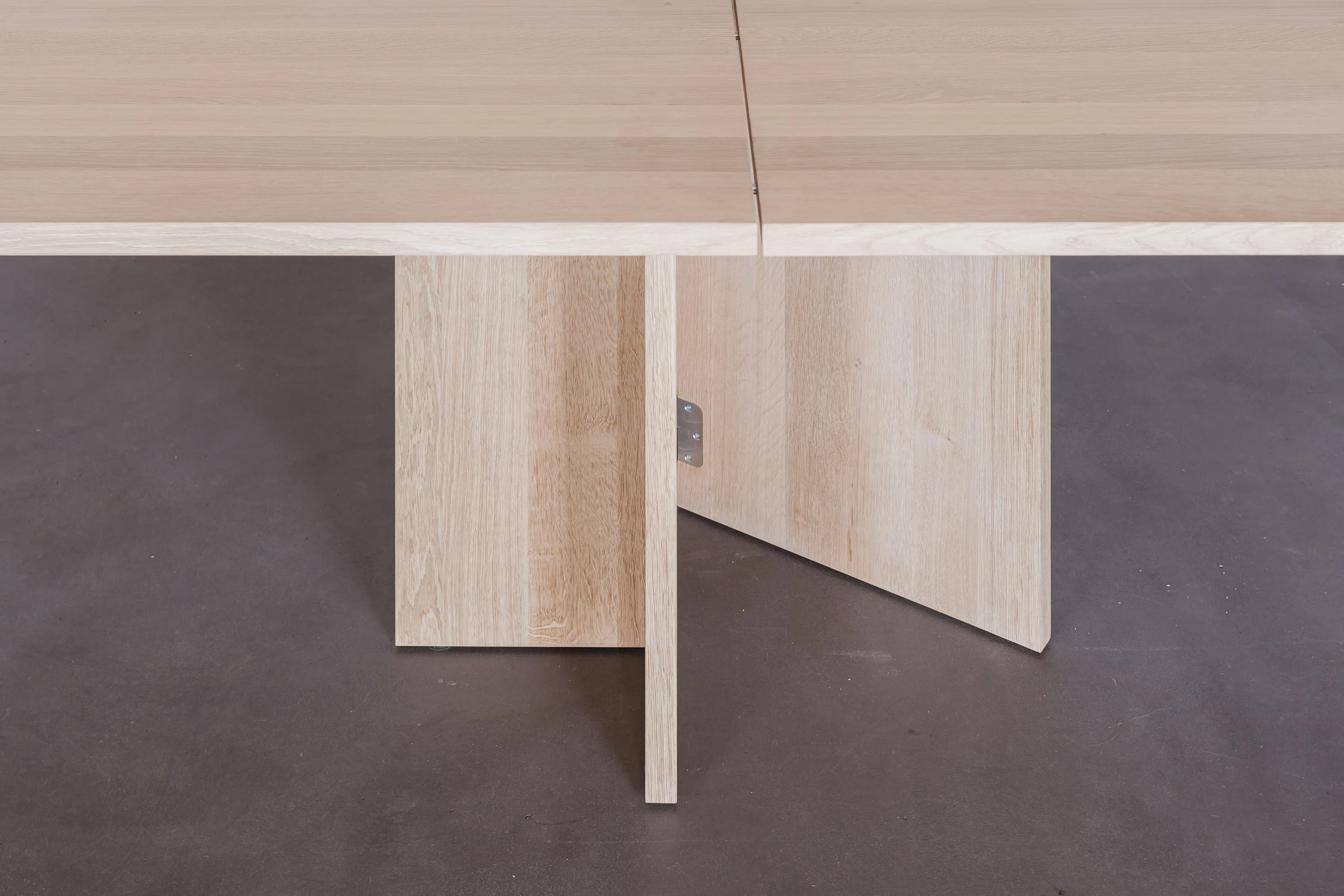 Kreuzförmiger Tischfuss aus Holz mit Metallscharnier unter der geteilten Tischplatte.