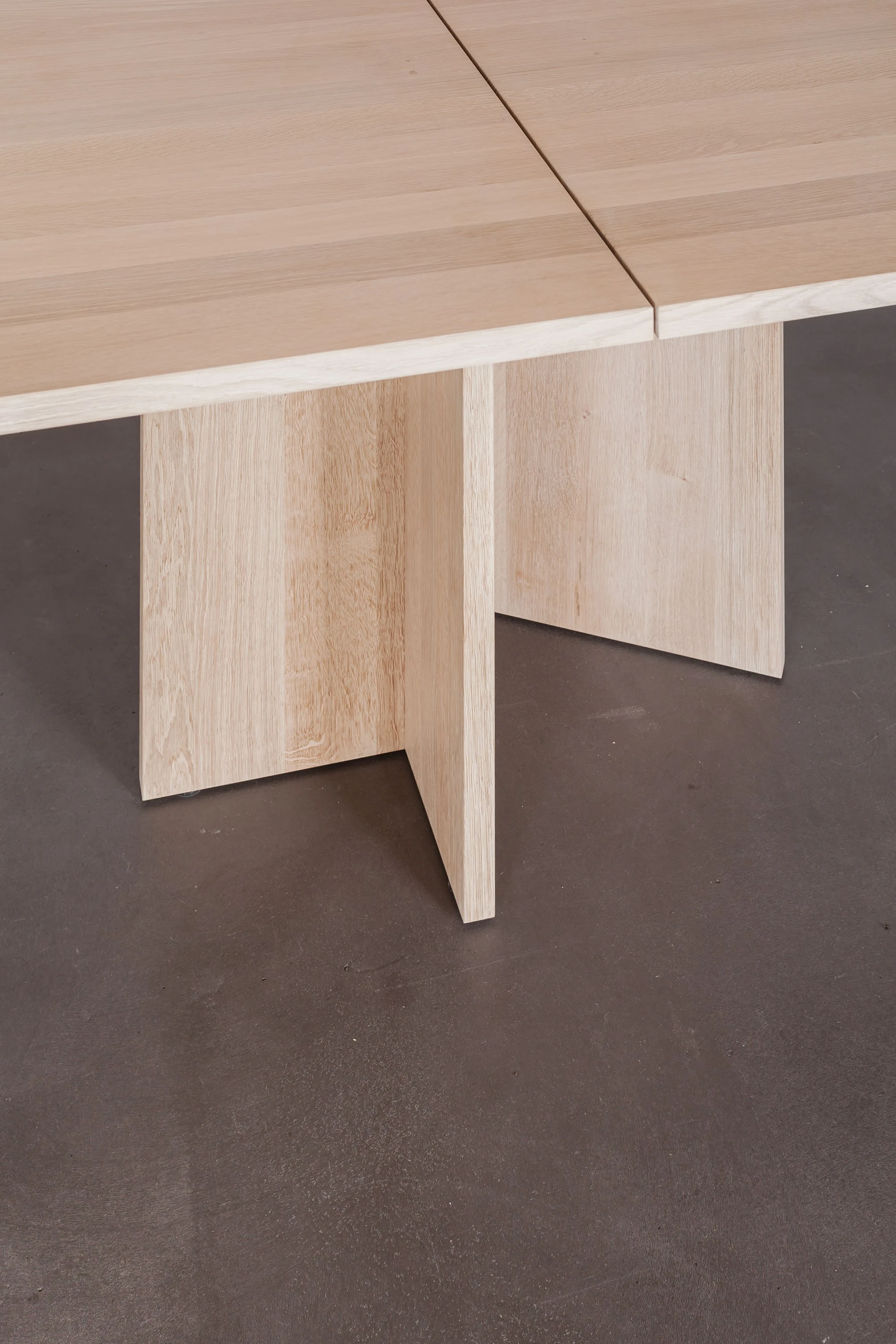 Kreuzförmiger Tischfuss aus Holz unter einer Tischplatte mit Mittelfuge.
