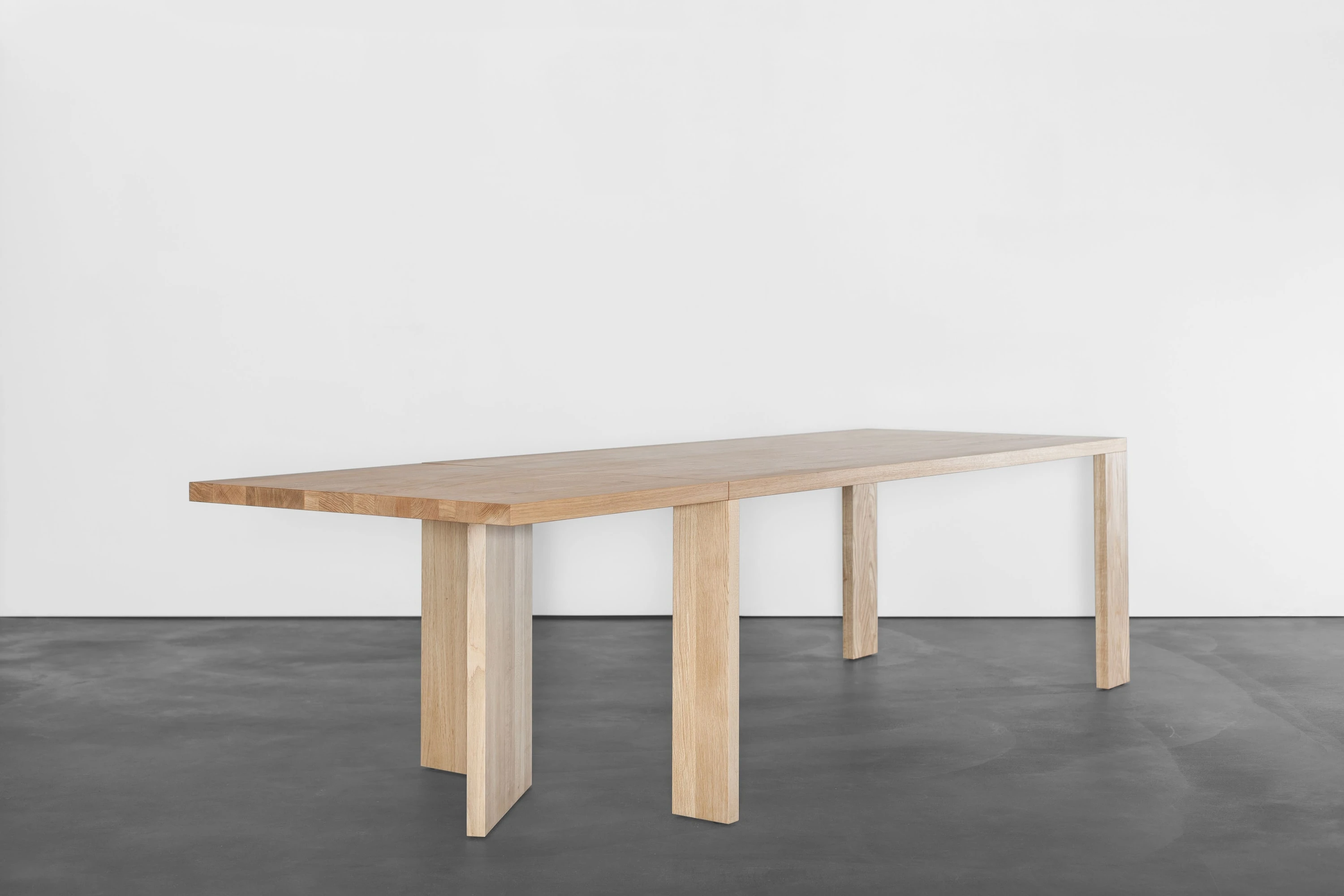 Langer Holztisch auf mehreren Plattenfüssen in Schrägansicht.