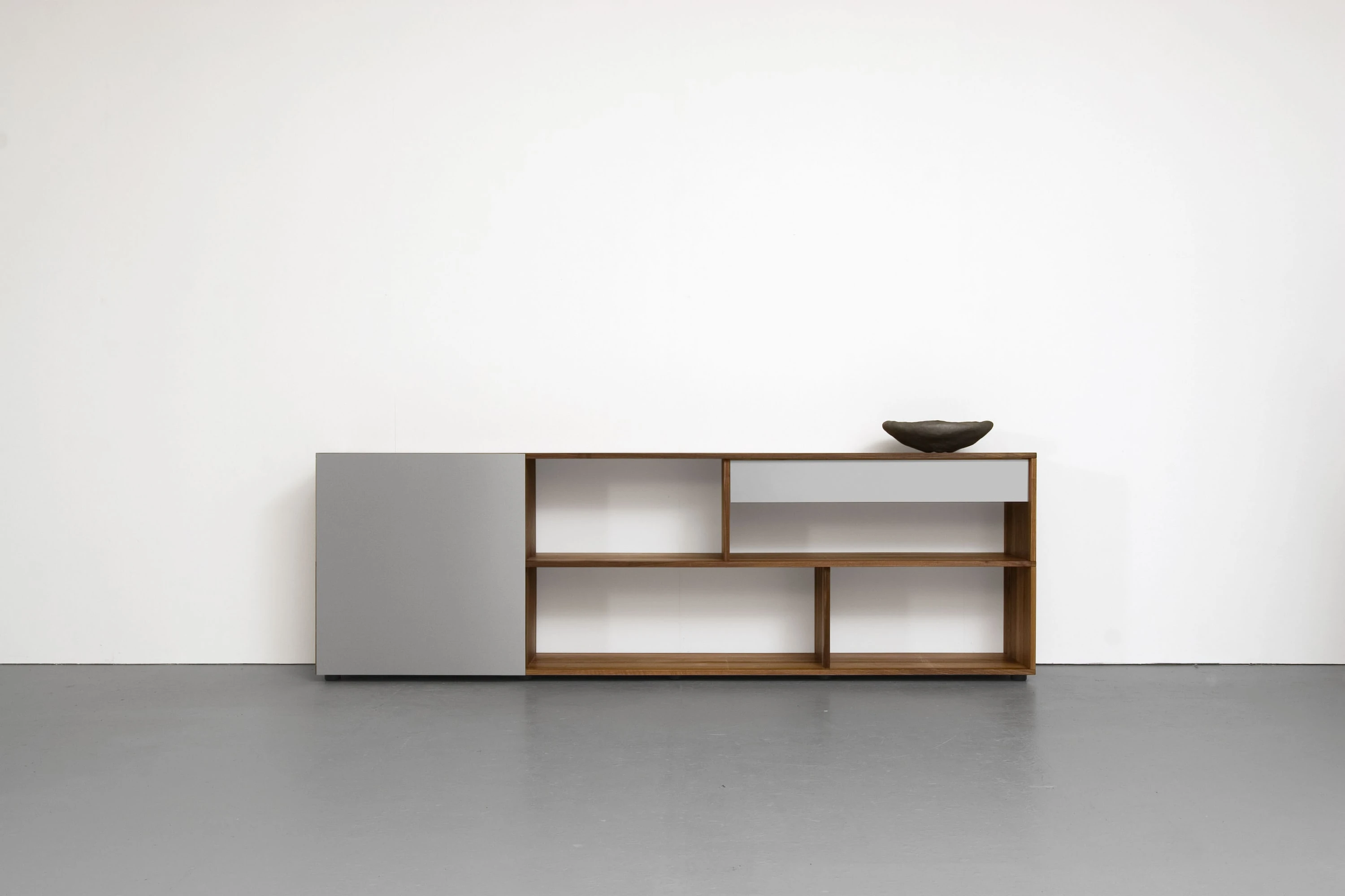 Sideboard aus Nussbaum mit offenen Fächern, grauen Schiebetüren und einer Schale obenauf.