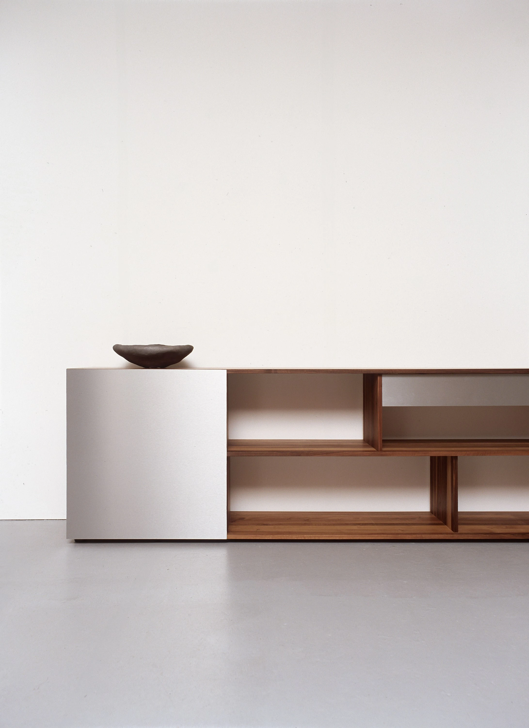 Sideboard mit hellgrauer Front und offenen Fächern aus dunklem Holz, darauf eine Schale.
