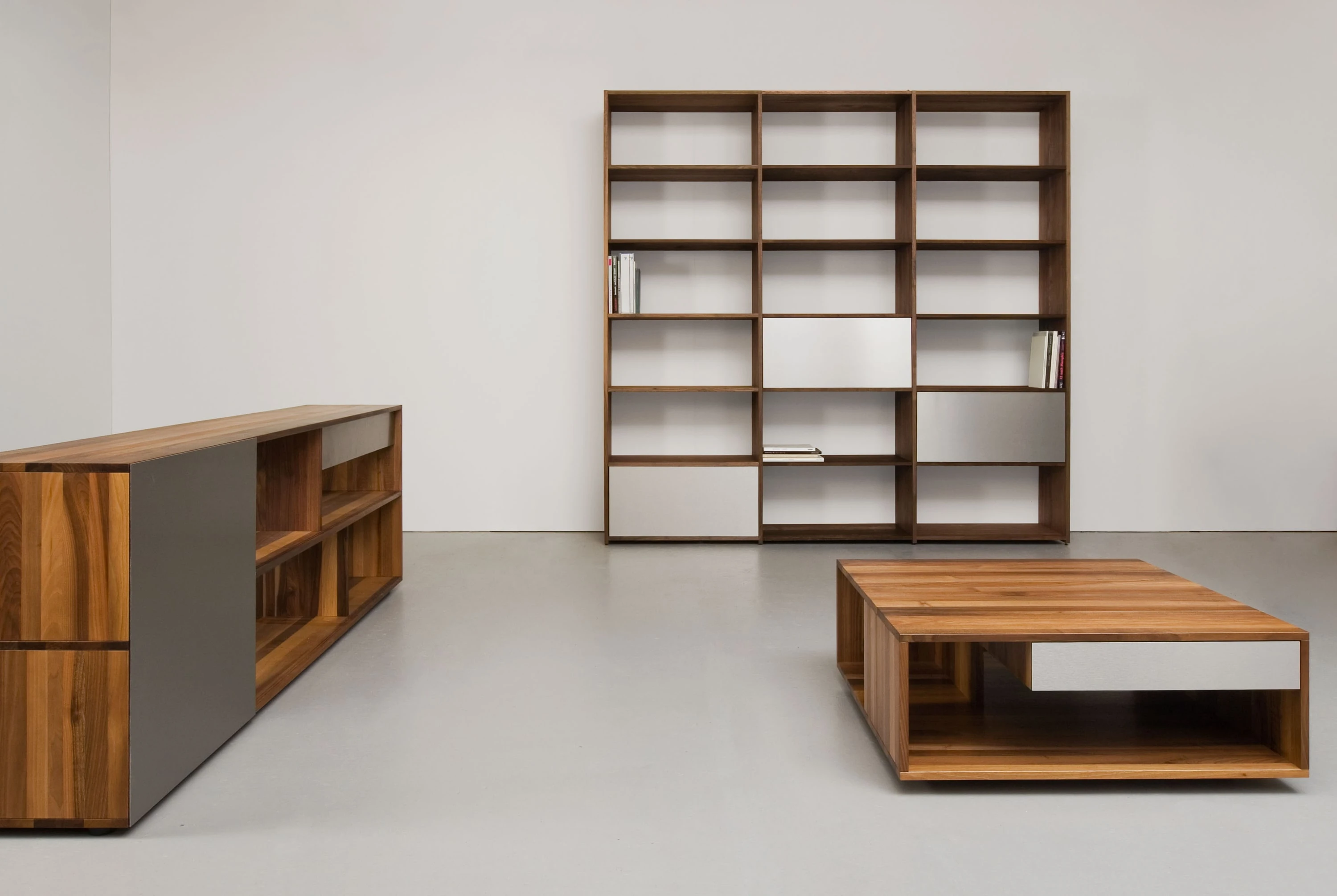 Sideboard und hohes Regal aus dunklem Holz mit grauen und weissen Fronten, davor ein niedriger Salontisch aus dunklem Holz.