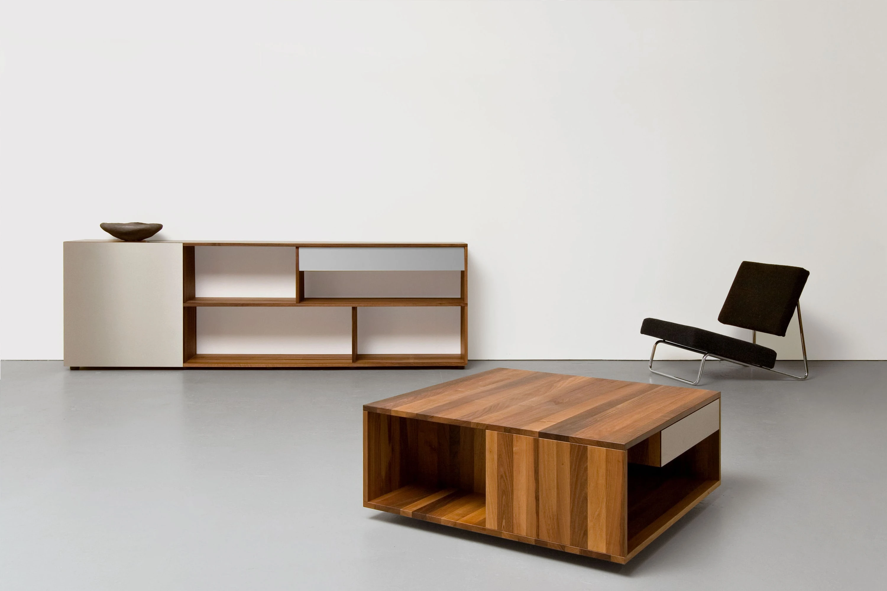 Sideboard mit hellen Fronten und Schale, davor ein Salontisch aus dunklem Holz und ein schwarzer Liegesessel.