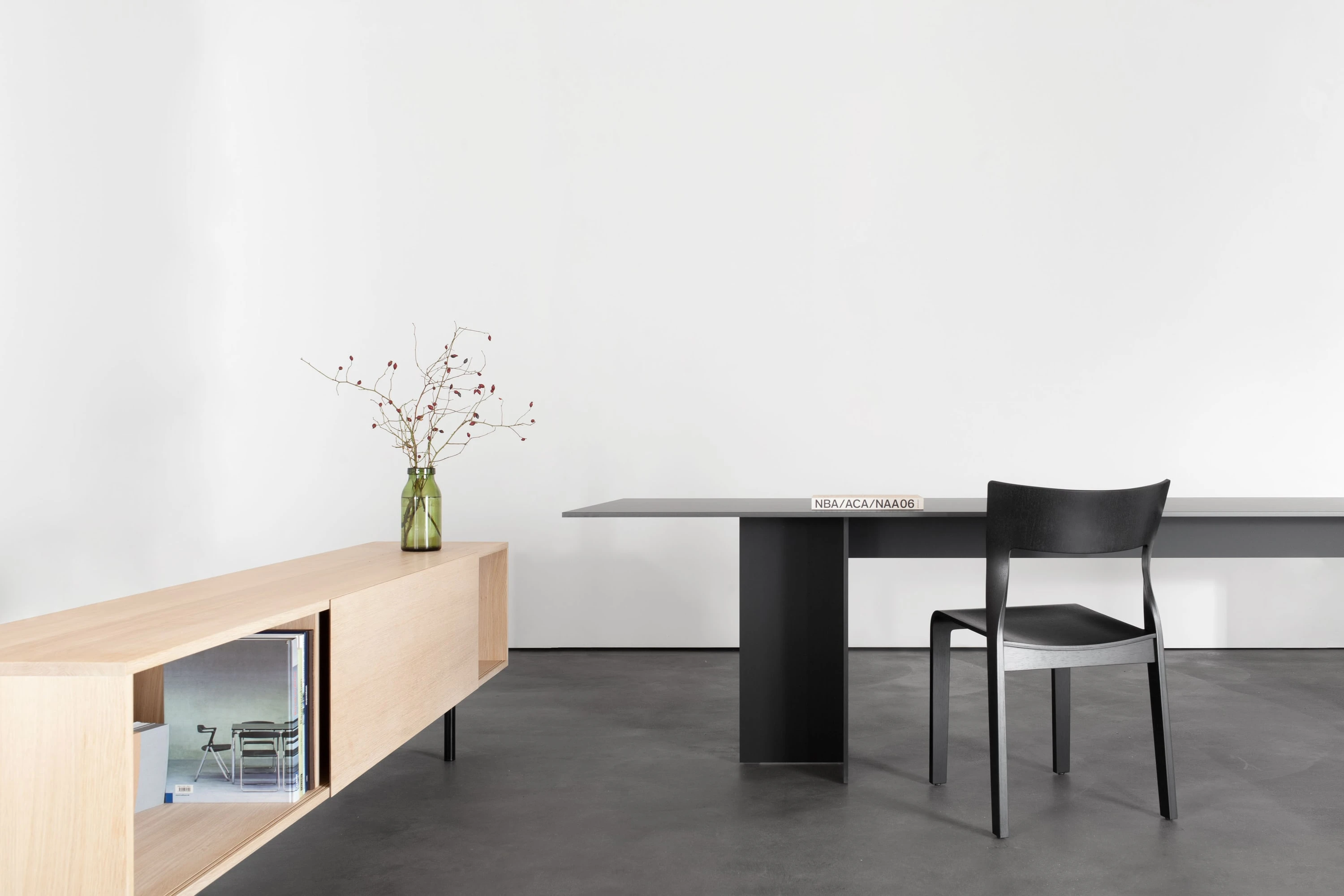 Sideboard aus Eiche mit Zweigen in einer Vase, dahinter ein schwarzer Tisch mit schwarzem Stuhl.