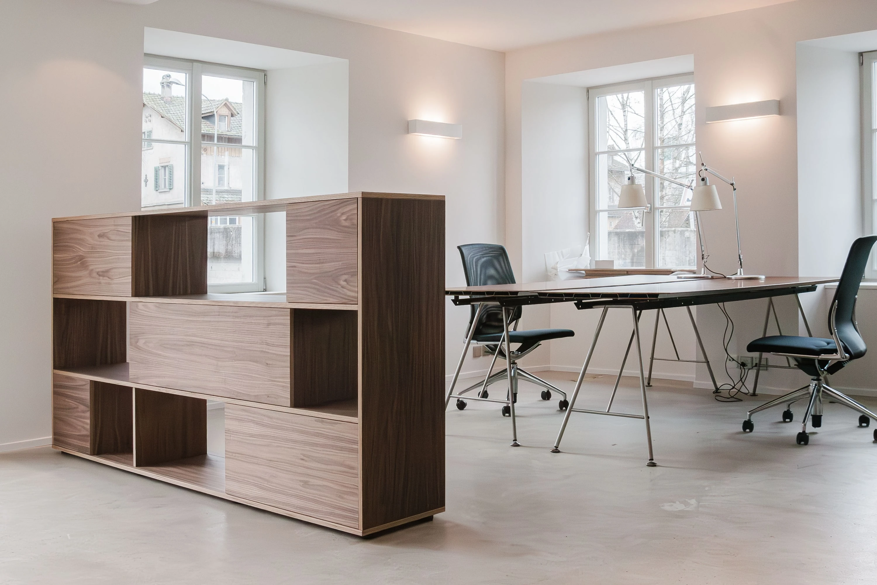Offenes Highboard aus Nussbaum als Raumteiler vor Arbeitsplätzen mit Drehstühlen.