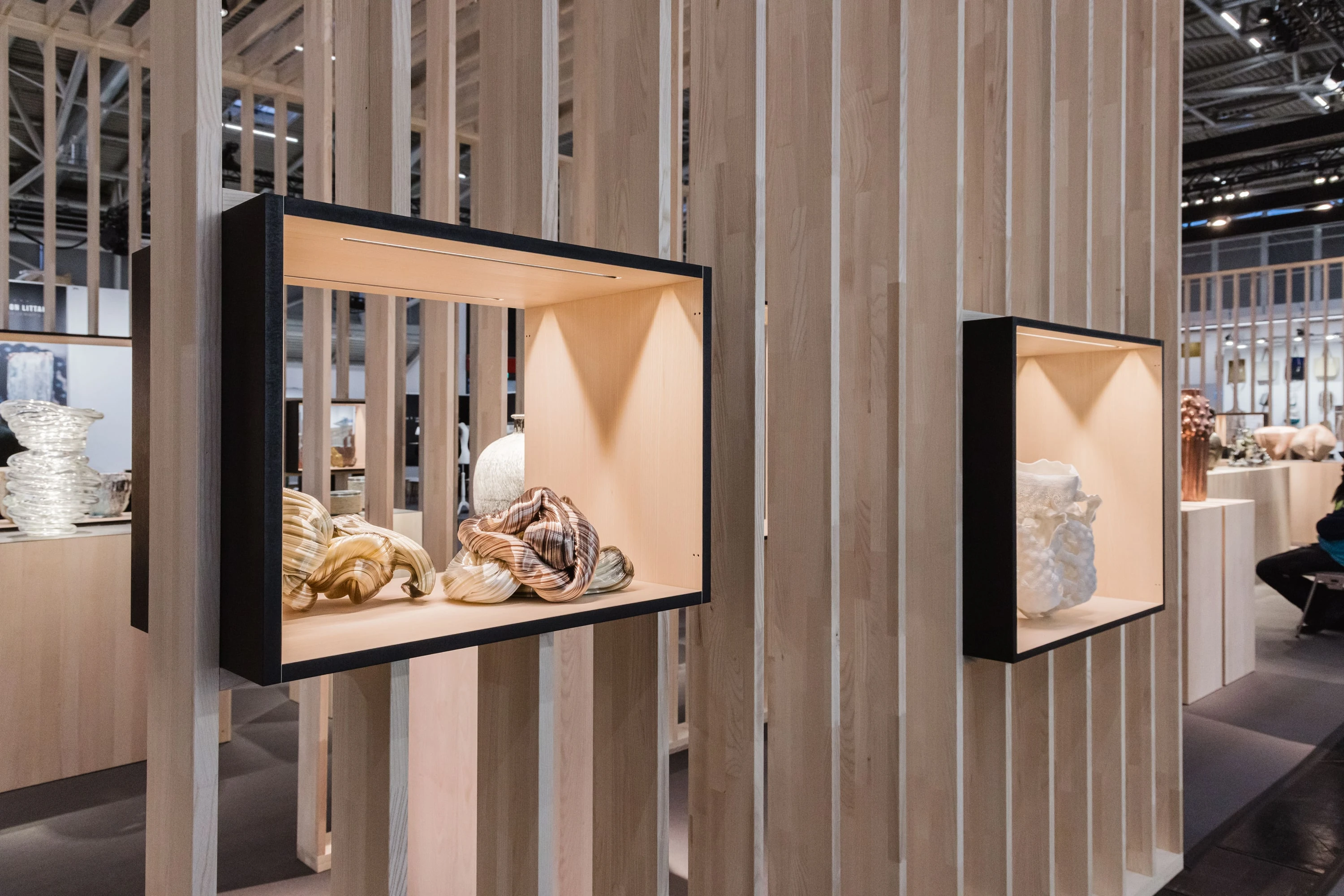 Nahaufnahme einer schwarz gerahmten Vitrine zwischen Holzlamellen mit Keramikobjekten, dahinter weitere Vitrinen.