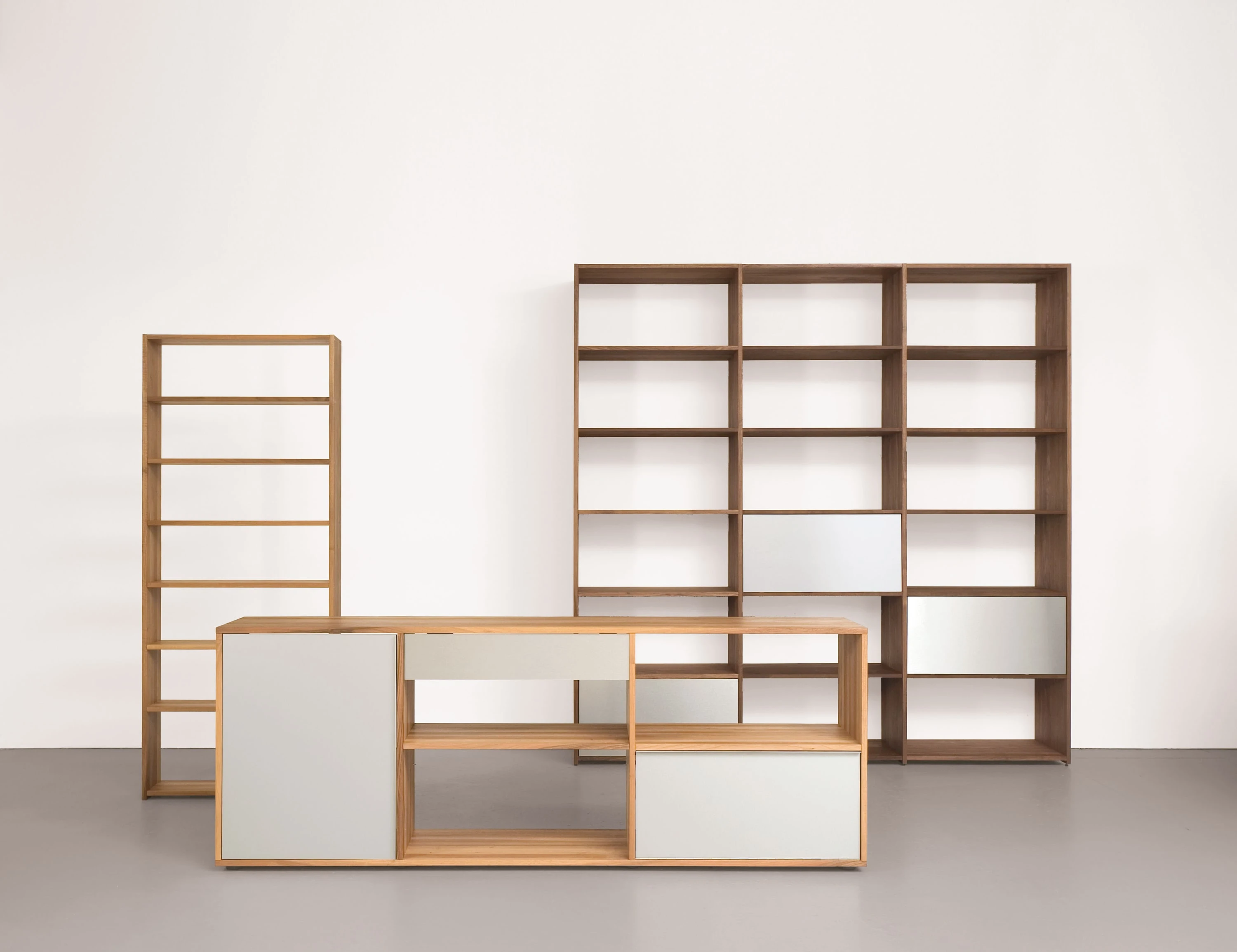 Schmales Regal und Sideboard aus Eiche mit grauen Fronten, dahinter ein breites Regal aus Nussbaum.