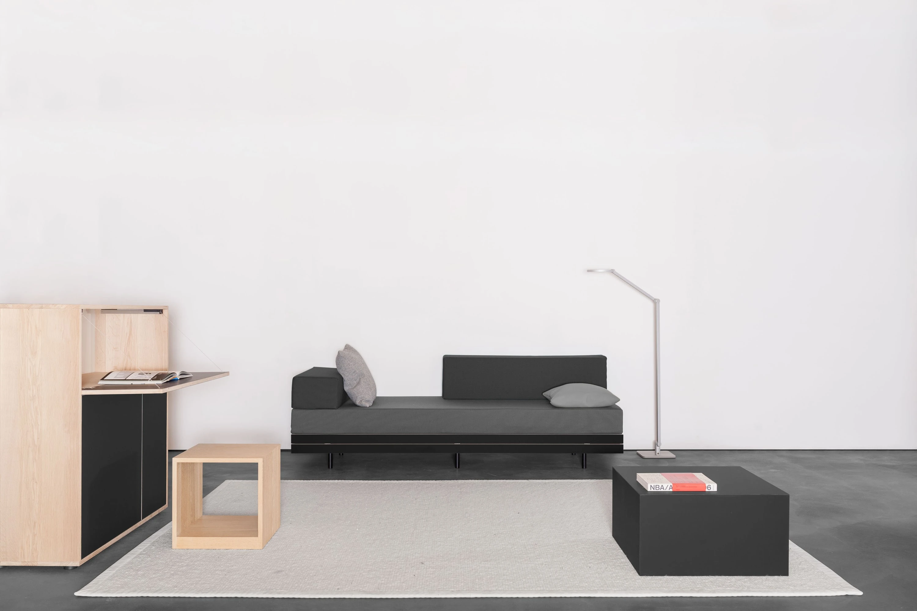 Sekretär aus Eiche mit aufgeklappter Schreibfläche, Holzhocker, dunkles Stapelbett und schwarzer Rollkubus auf hellem Teppich.