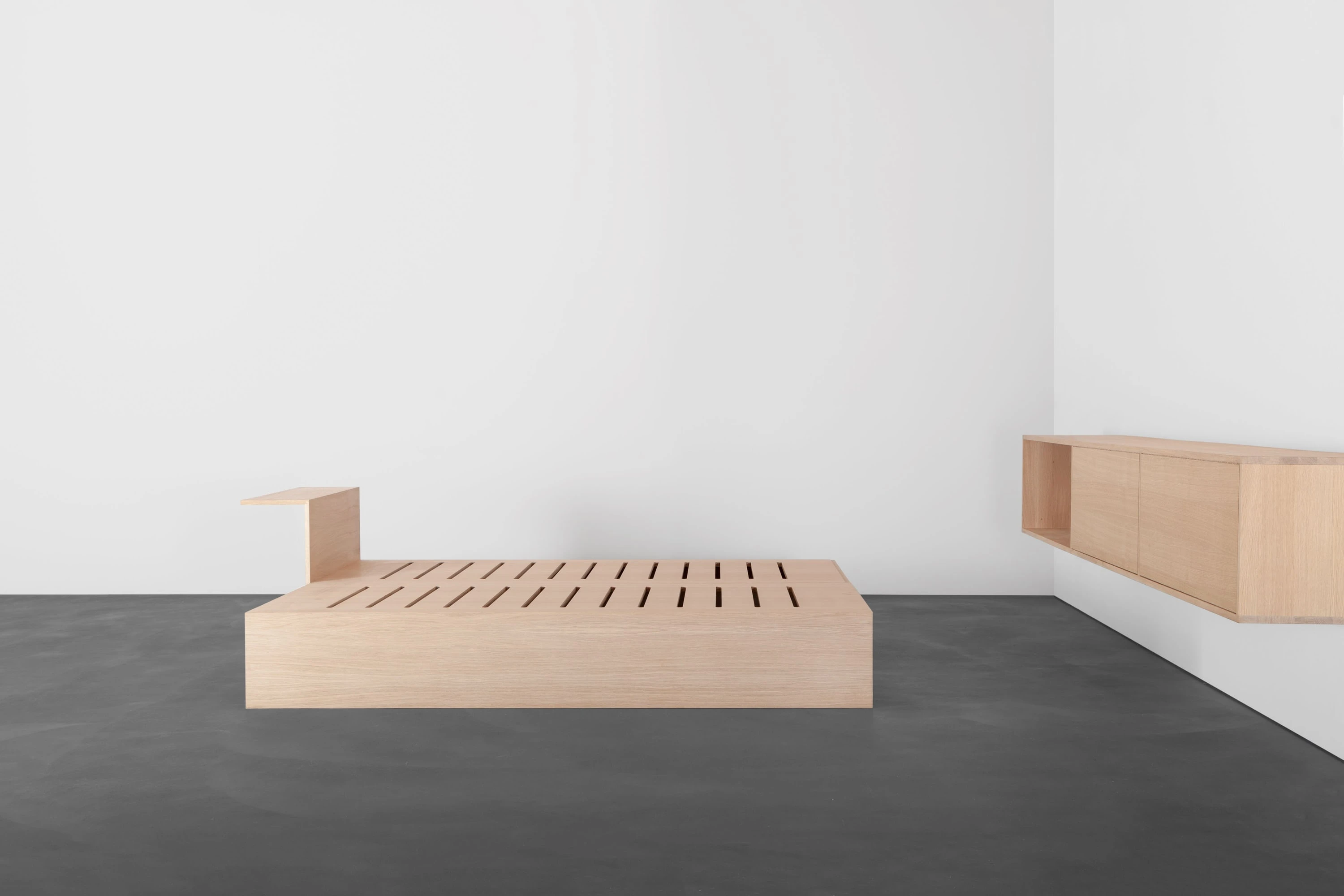 Couch aus Eiche ohne Polster mit sichtbarem Lattenrost, rechts ein Wandregal aus Eiche.