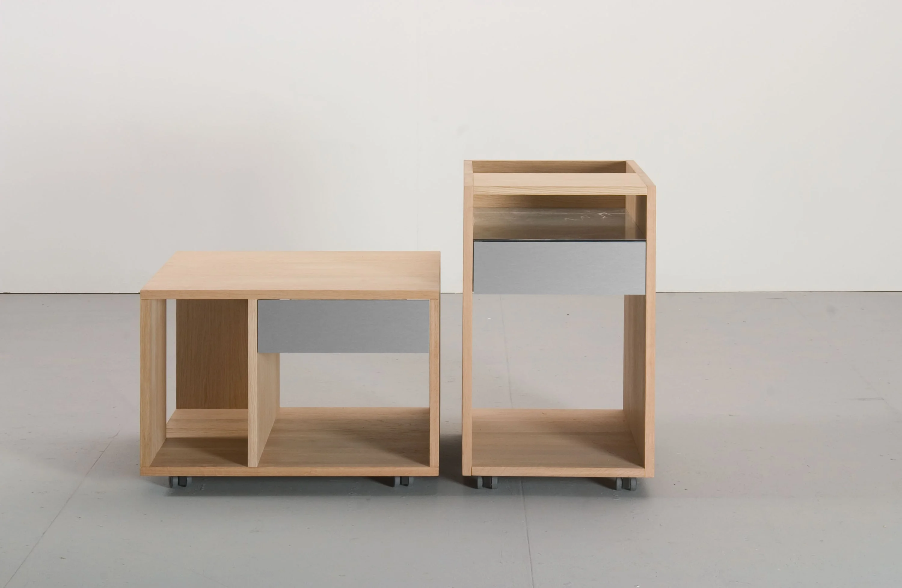 Zwei Rollcontainer aus hellem Holz mit grauer Schublade, ein niedriger und ein hoher.