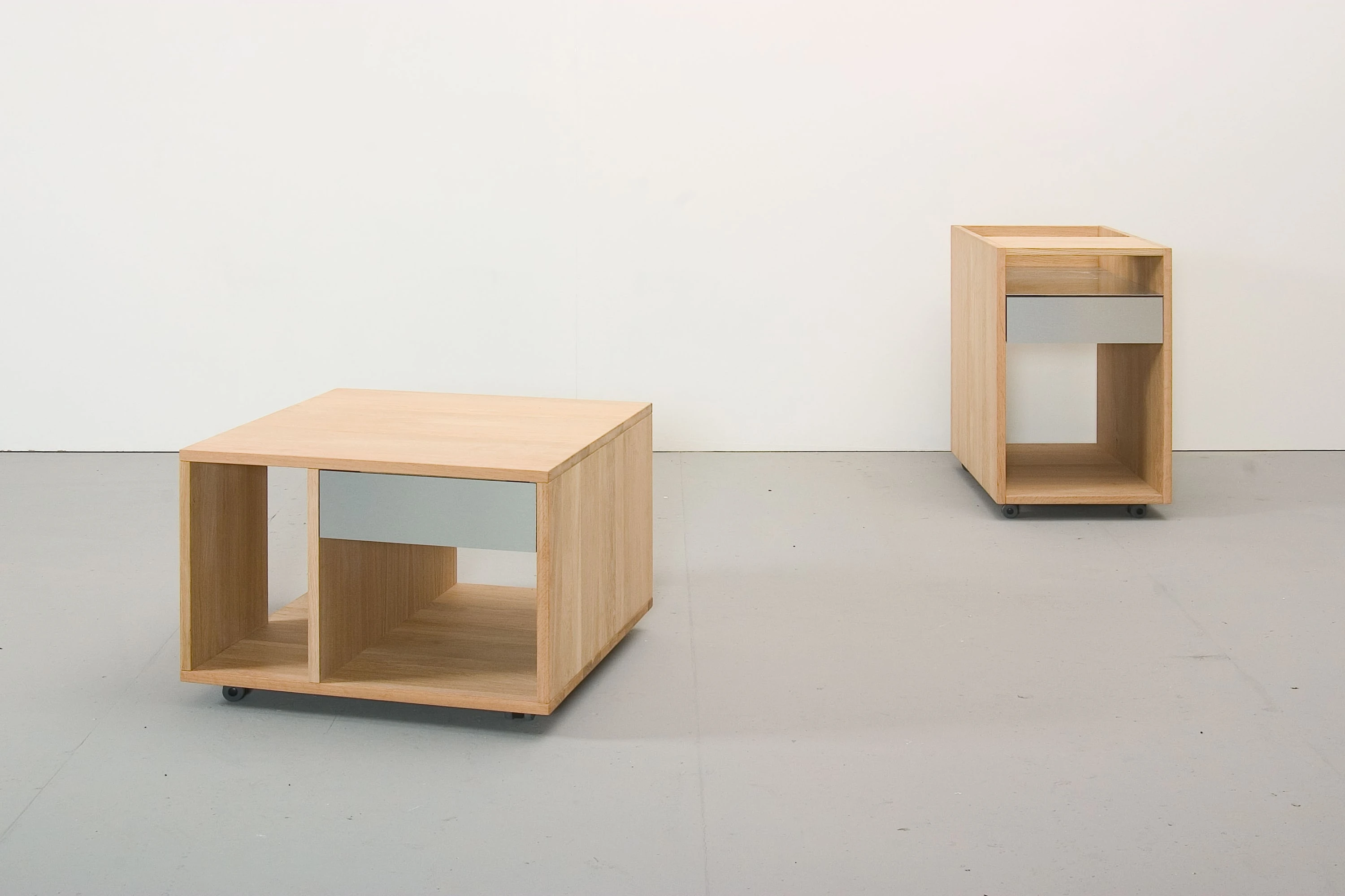 Niedriger Rollcontainer aus hellem Holz mit grauer Schublade, dahinter ein hoher.