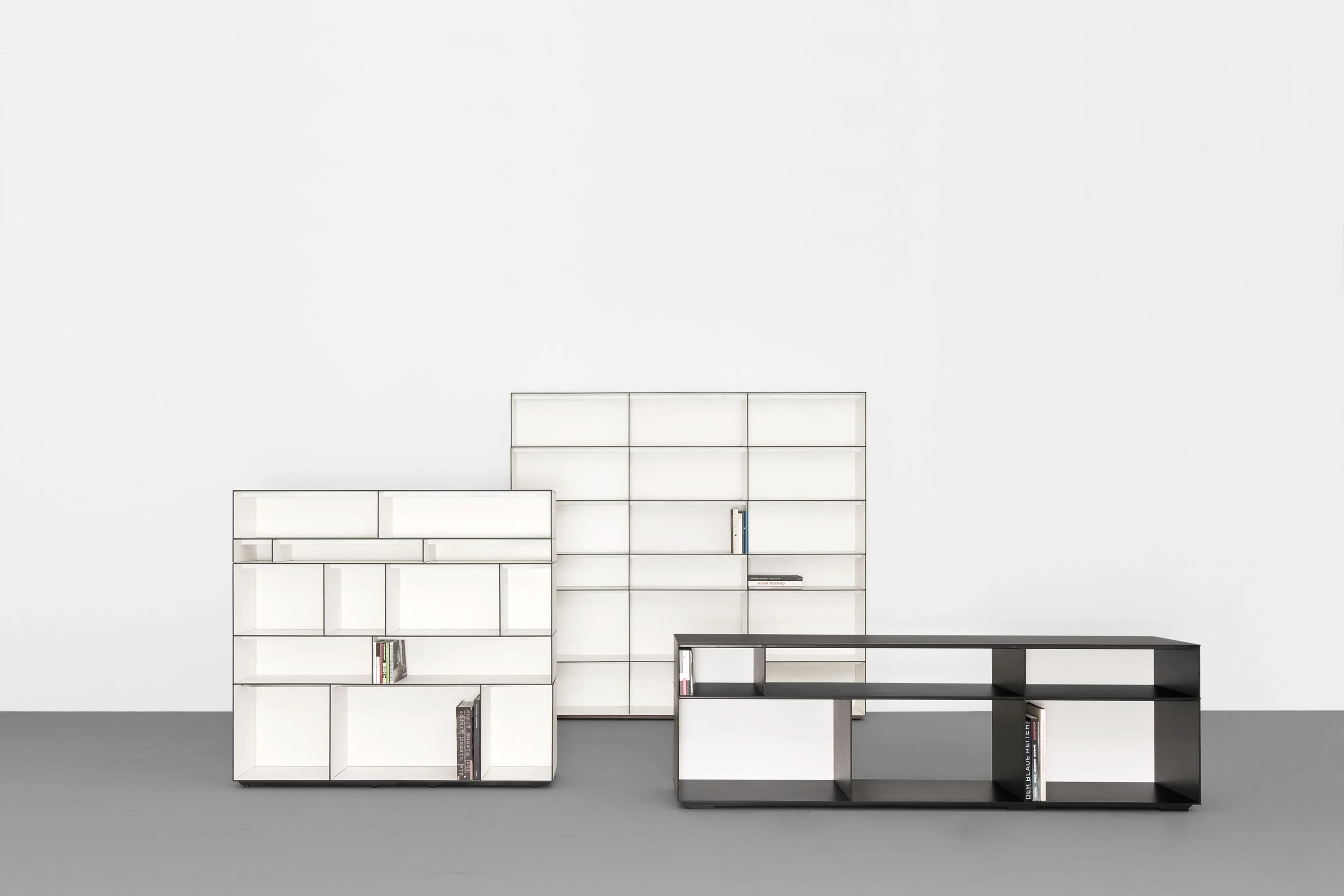 Zwei weisse Regale unterschiedlicher Höhe und ein schwarzes Sideboard mit Büchern.