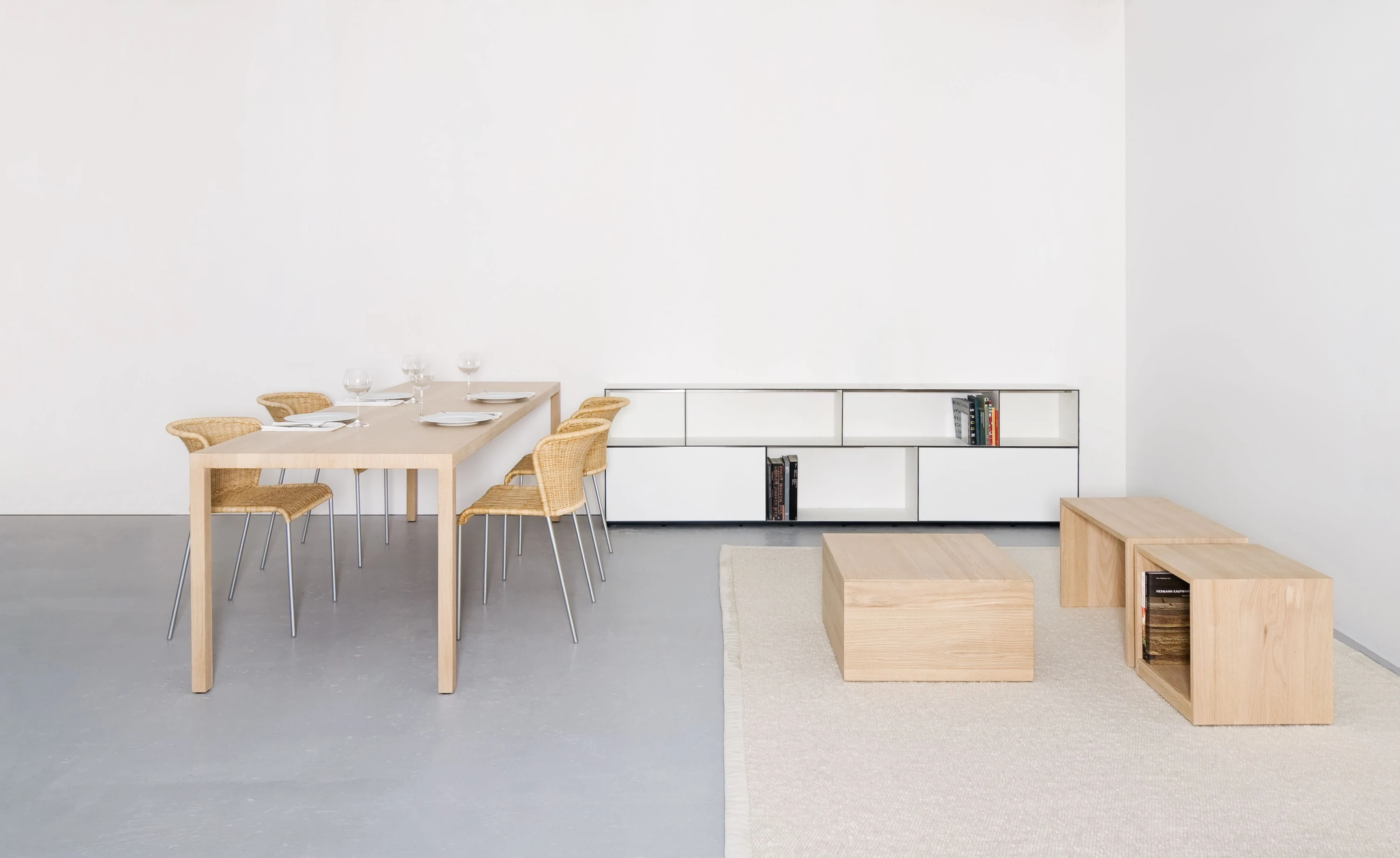 Gedeckter Esstisch aus Eiche mit Geflechtstühlen, dahinter ein langes weisses Sideboard, rechts Holzkuben auf hellem Teppich.