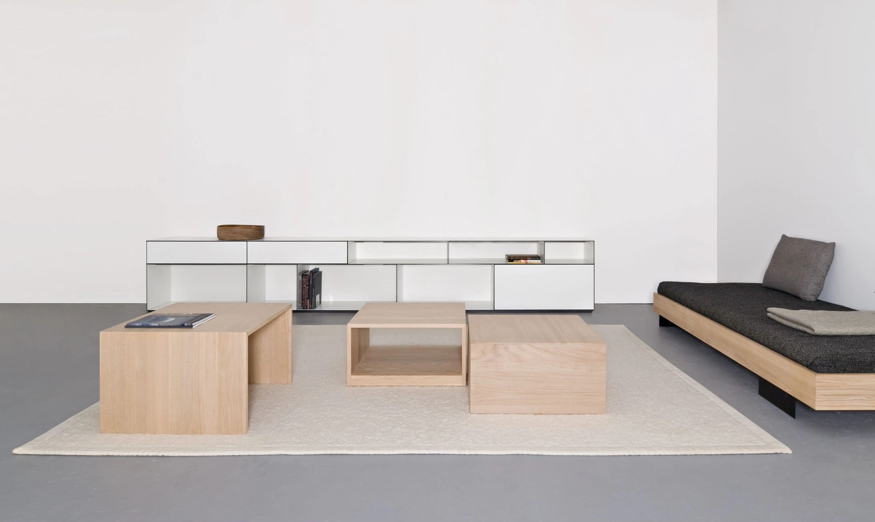 Langes weisses Sideboard, davor niedrige Holztische auf hellem Teppich, rechts eine Tagesliege mit dunkler Auflage.