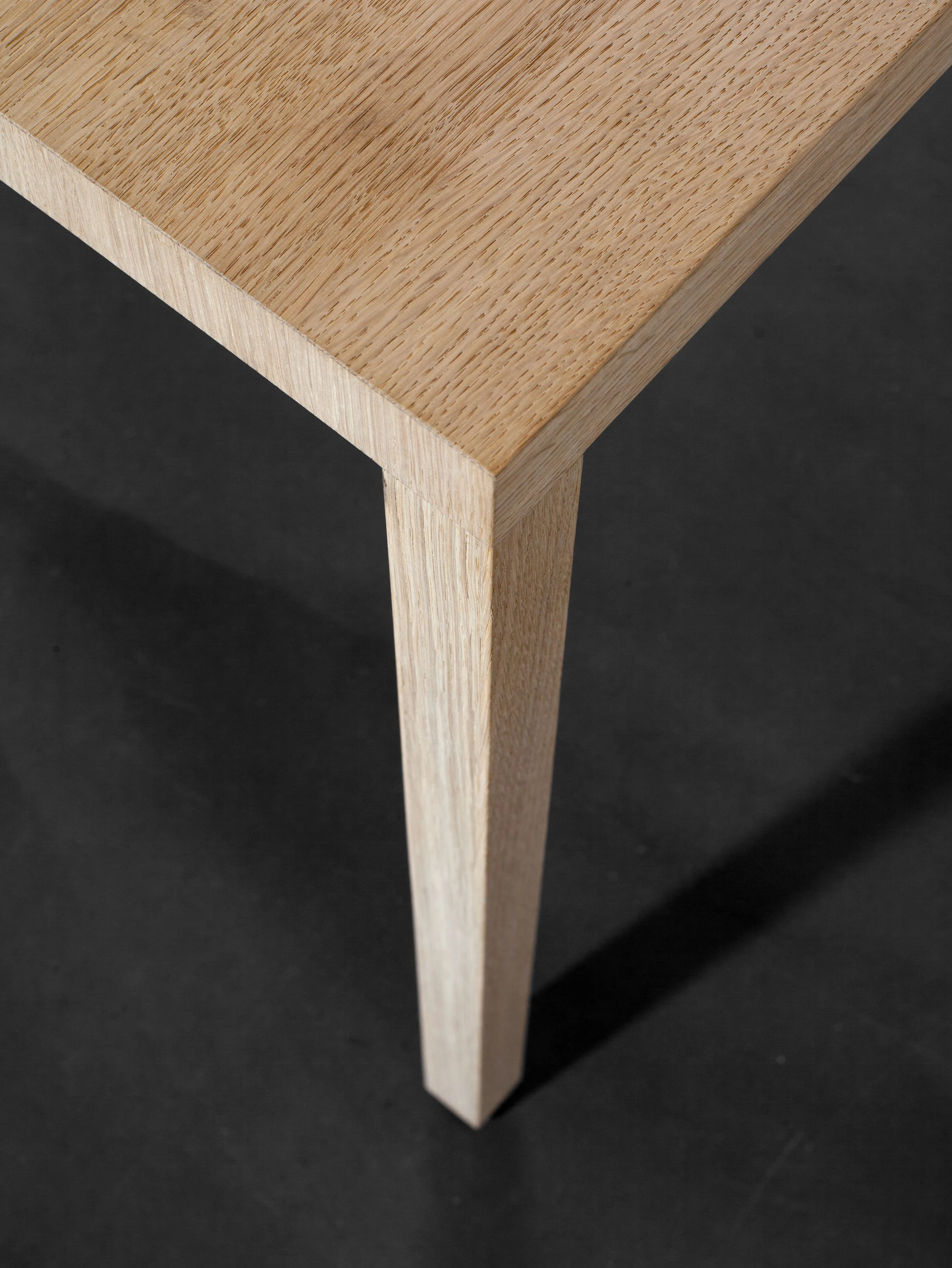 Nahaufnahme einer Tischecke aus Holz mit sich verjüngendem Bein vor dunklem Hintergrund.