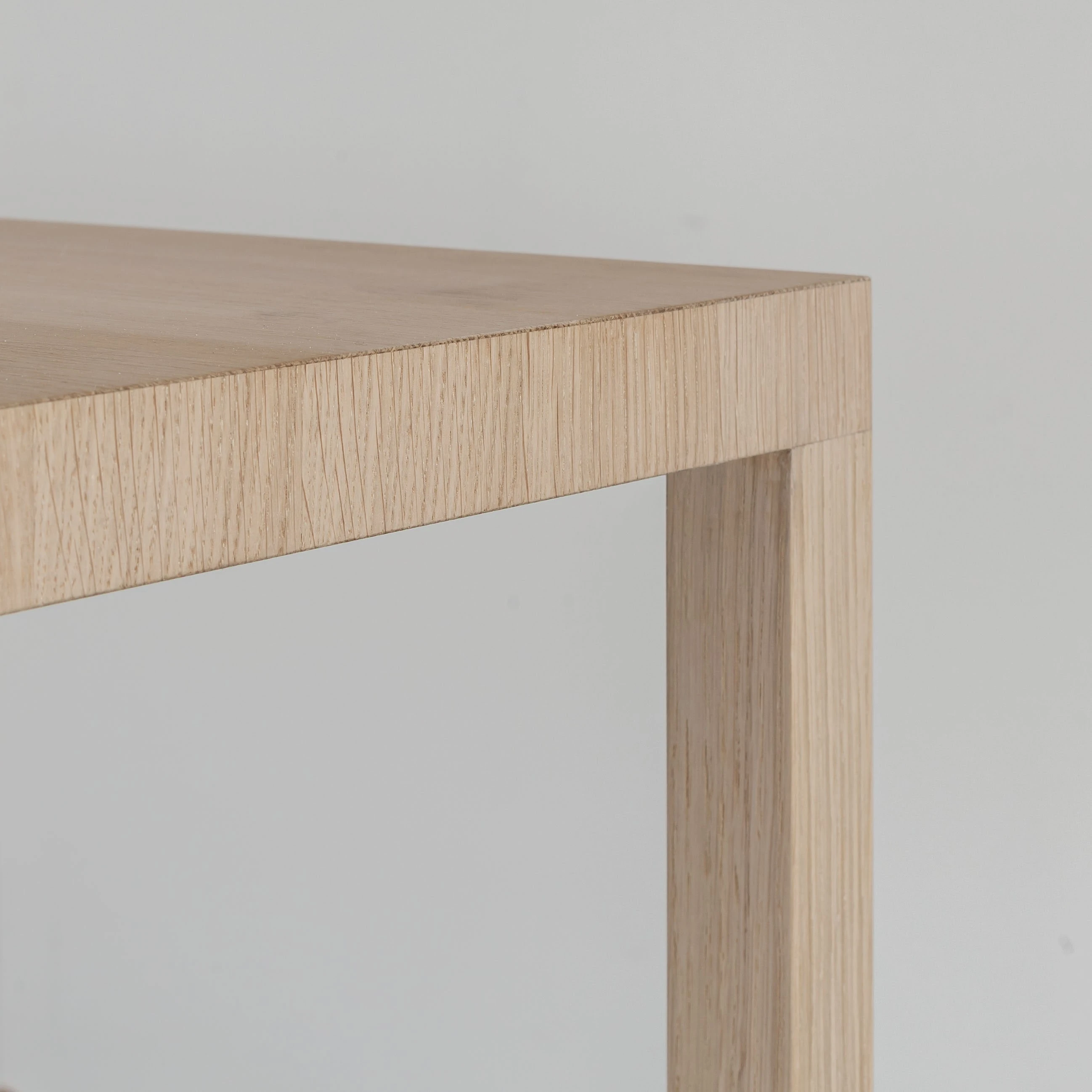 Nahaufnahme einer Tischecke aus hellem Holz mit Bein und Plattenkante.
