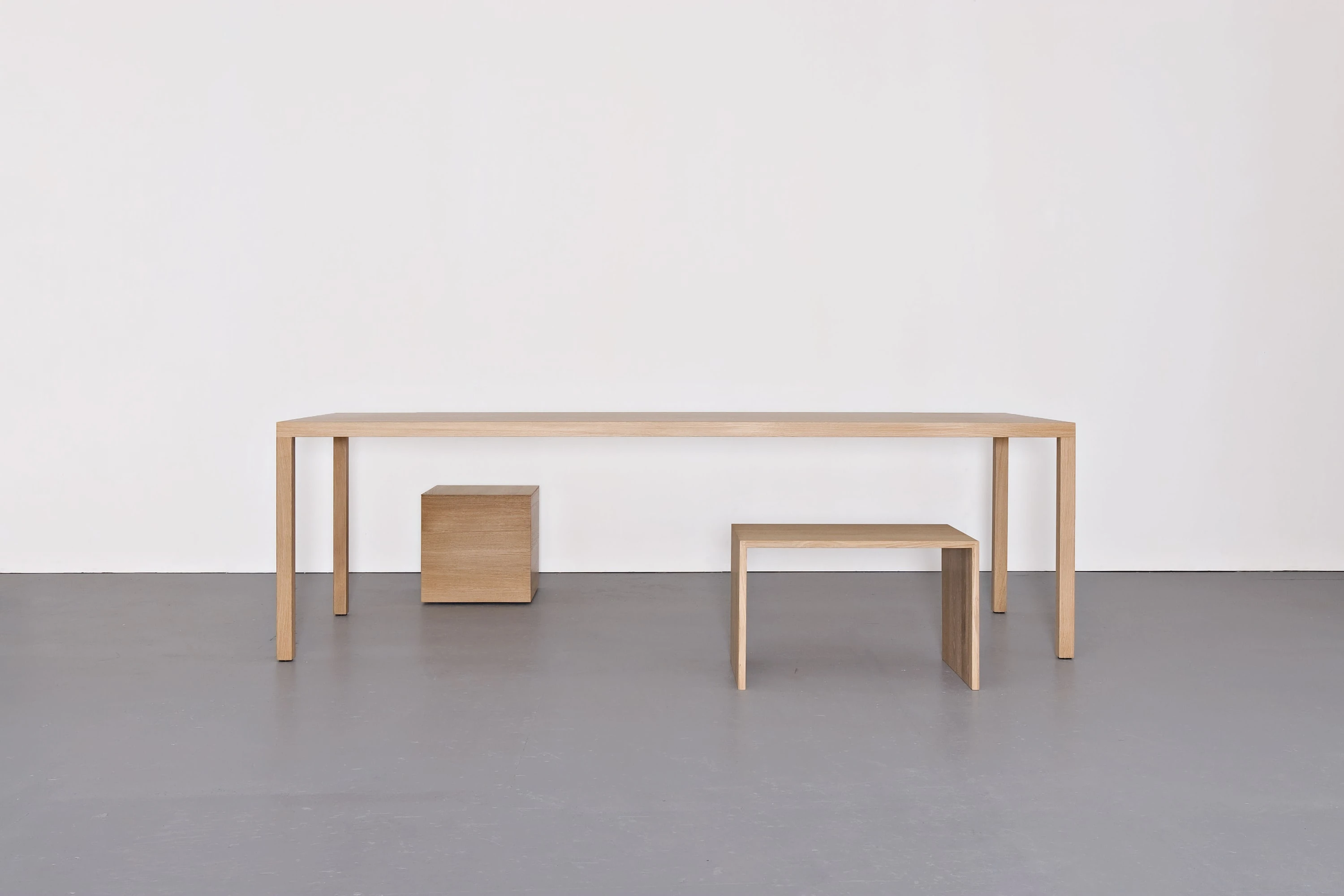 Schlichter Holztisch mit einem Holzkubus und einem Hocker darunter.