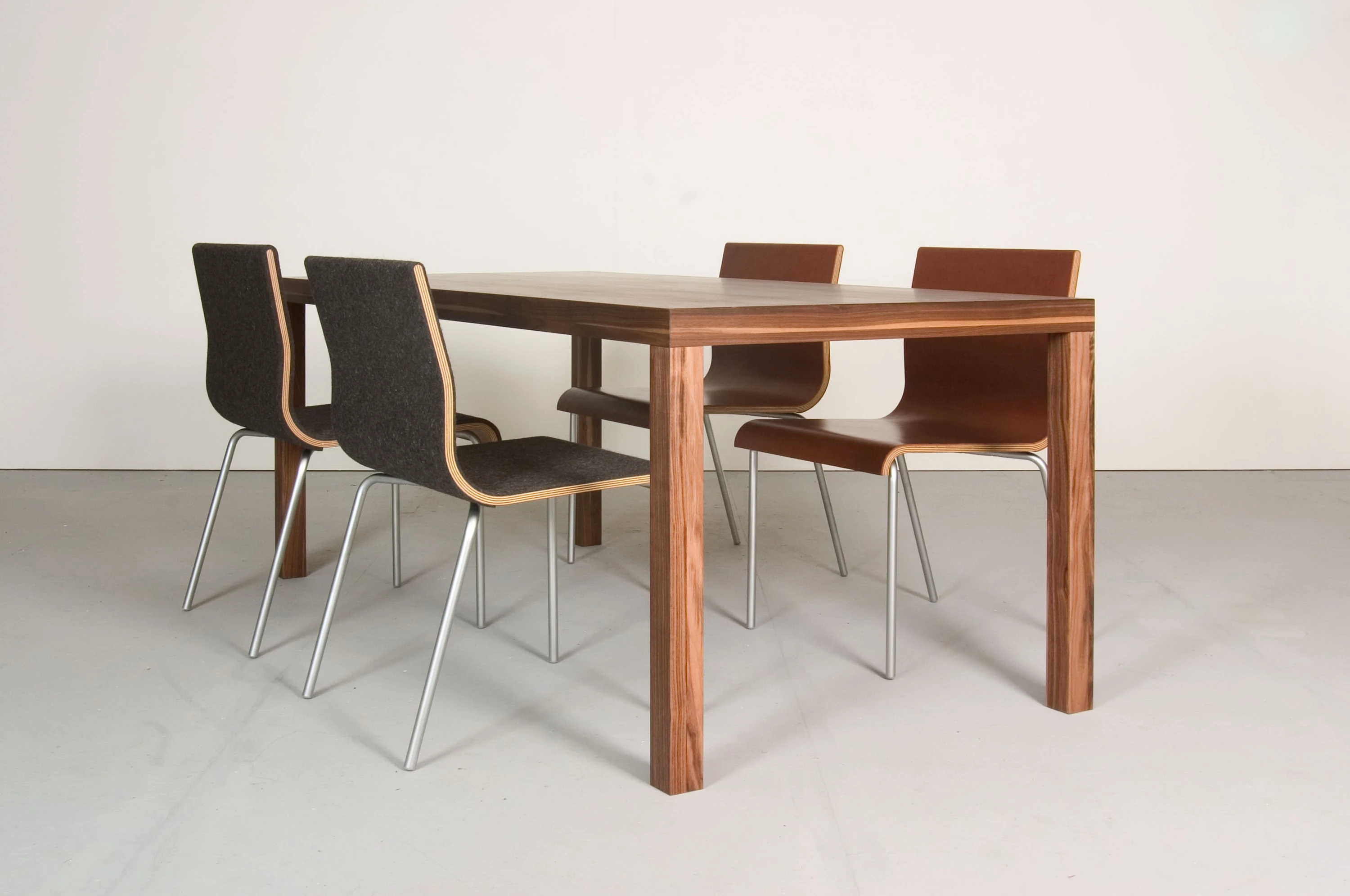 Tisch aus dunklem Holz mit vier Stühlen auf Stahlbeinen.