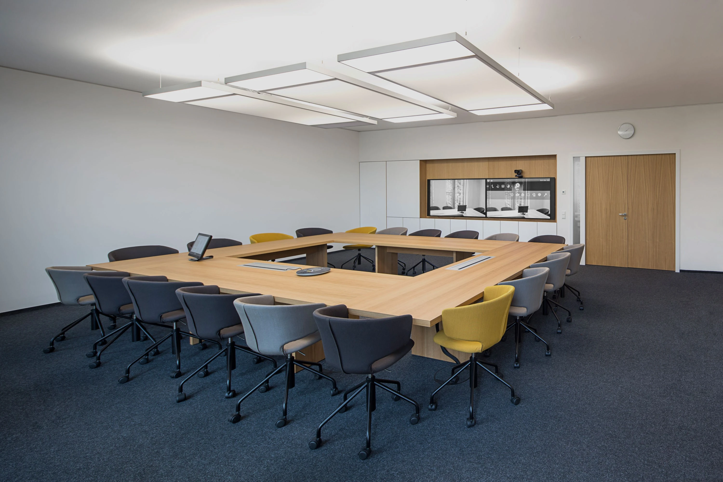 Conference room with a large U-shaped table, gray and yellow chairs and acoustic ceiling panels.