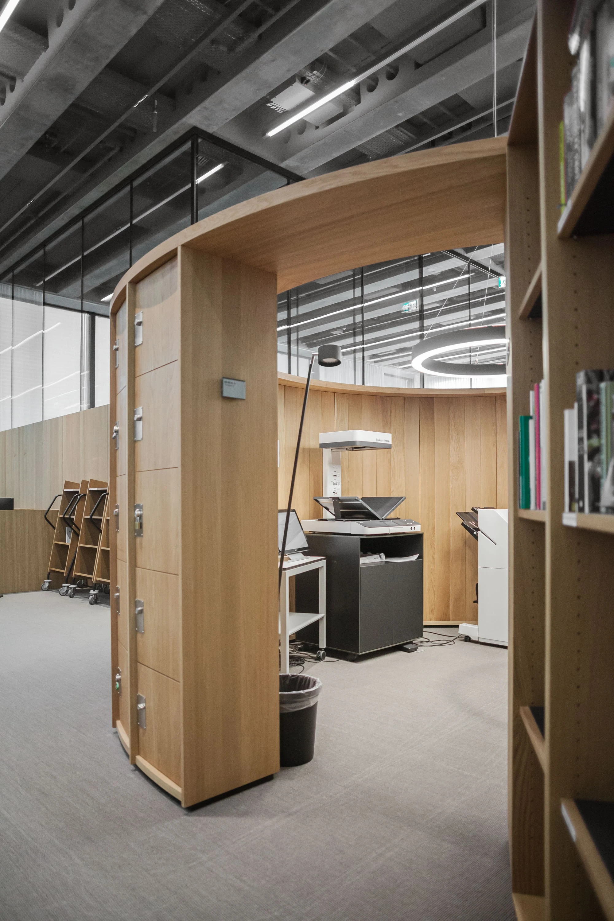Runder Einbau aus Holz mit Kopierer und Rollmöbel unter einer dunklen Decke.