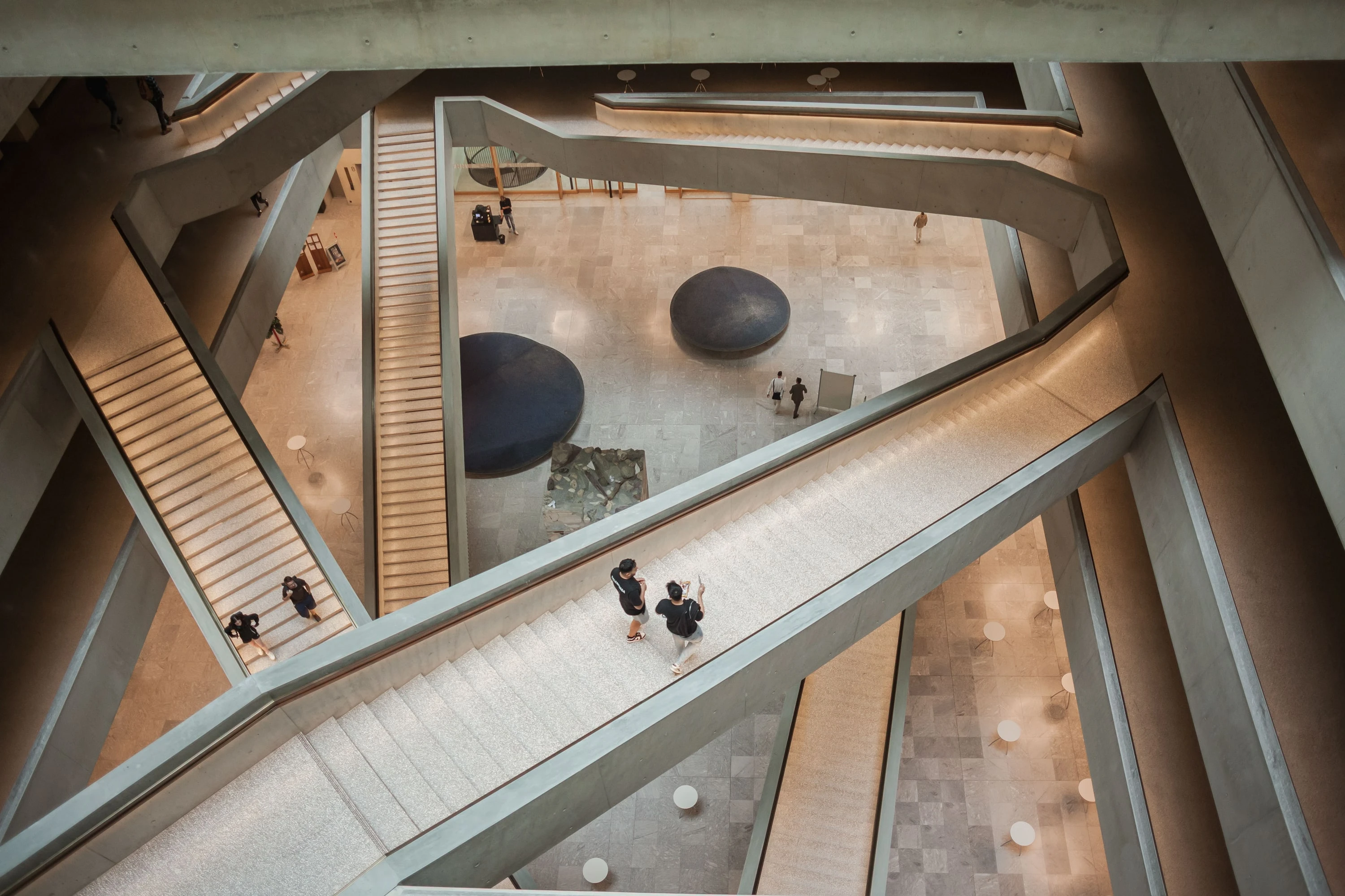 Aufsicht auf das Atrium mit sich kreuzenden Treppenläufen und Menschen.