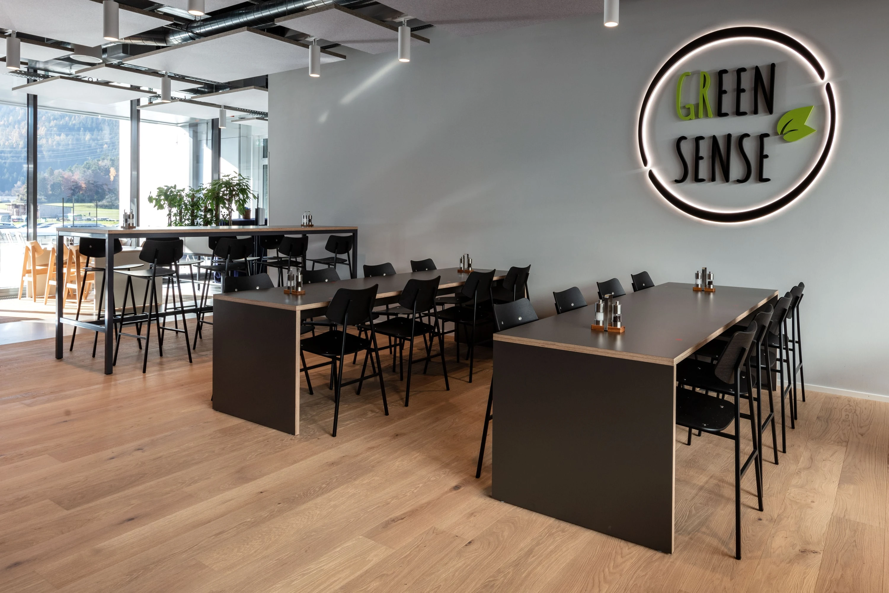 Restaurantbereich mit dunklen Hochtischen, Barhockern und beleuchtetem Schriftzug an der Wand.