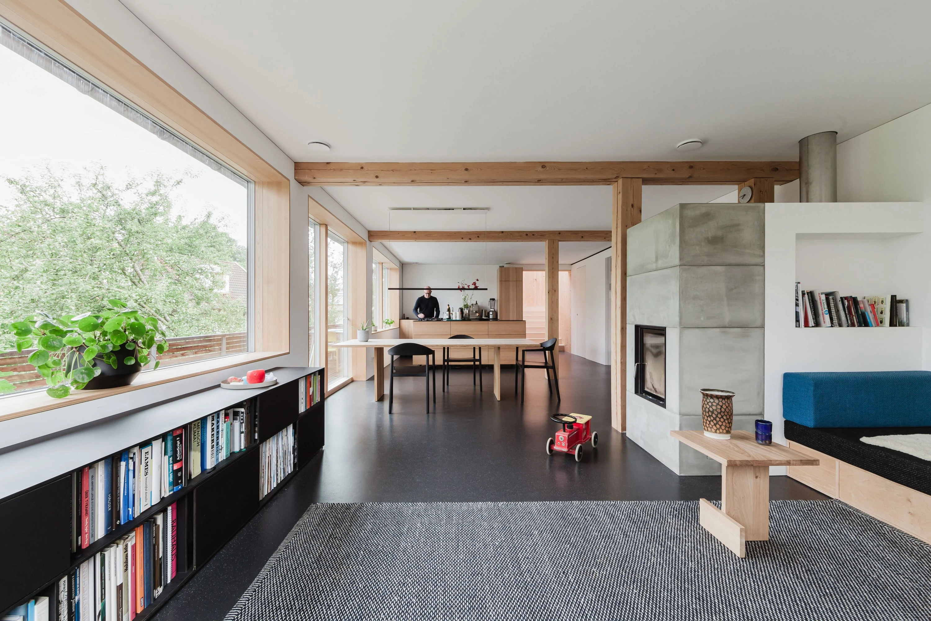 Offener Wohnbereich mit Bücherregal und Kamin, im Hintergrund der Essbereich.