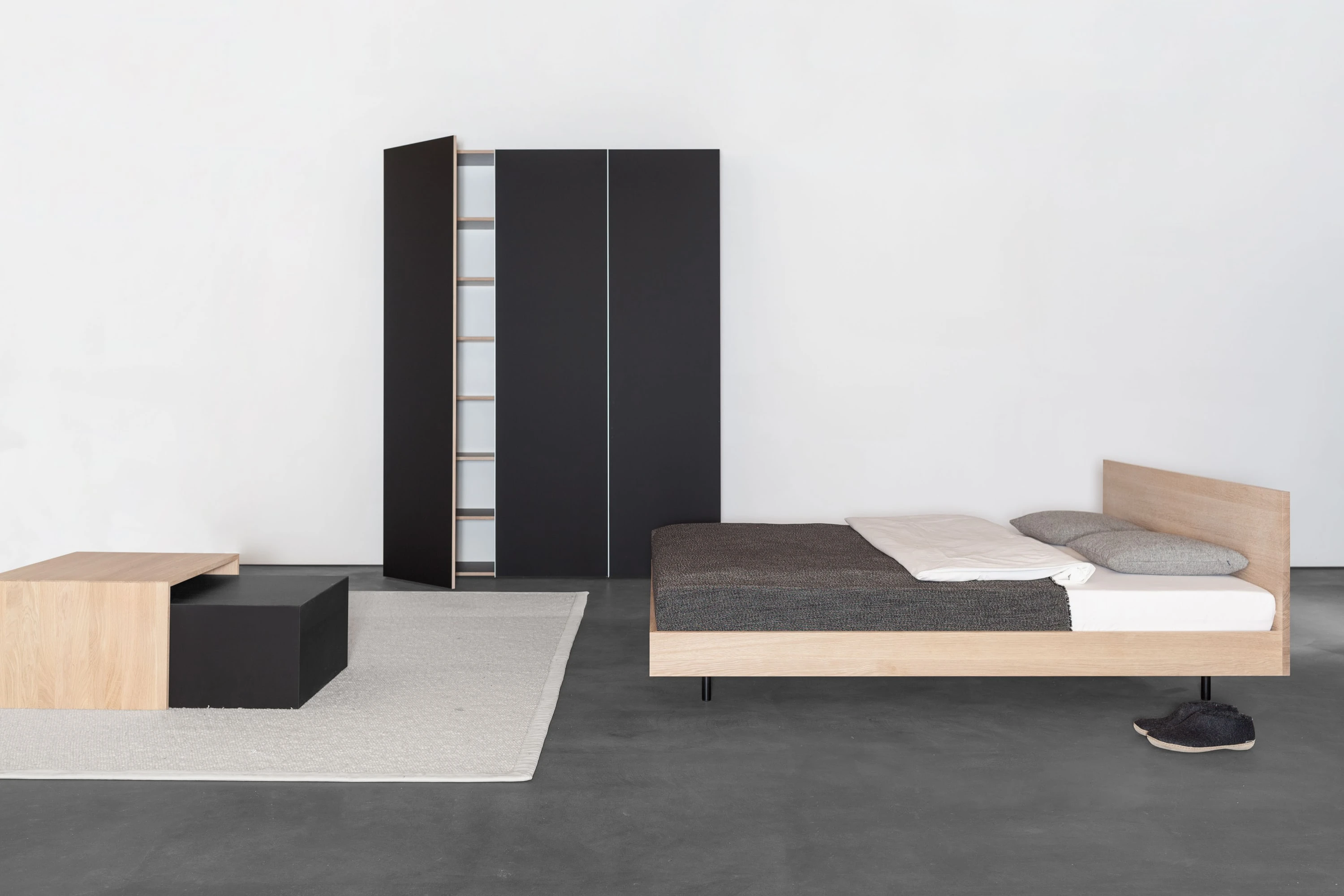 Schlafzimmer mit schwarzem Schrank, Salontisch aus Holz und schwarzem Kasten auf hellem Teppich und Bett aus Eiche mit hohem Kopfteil.