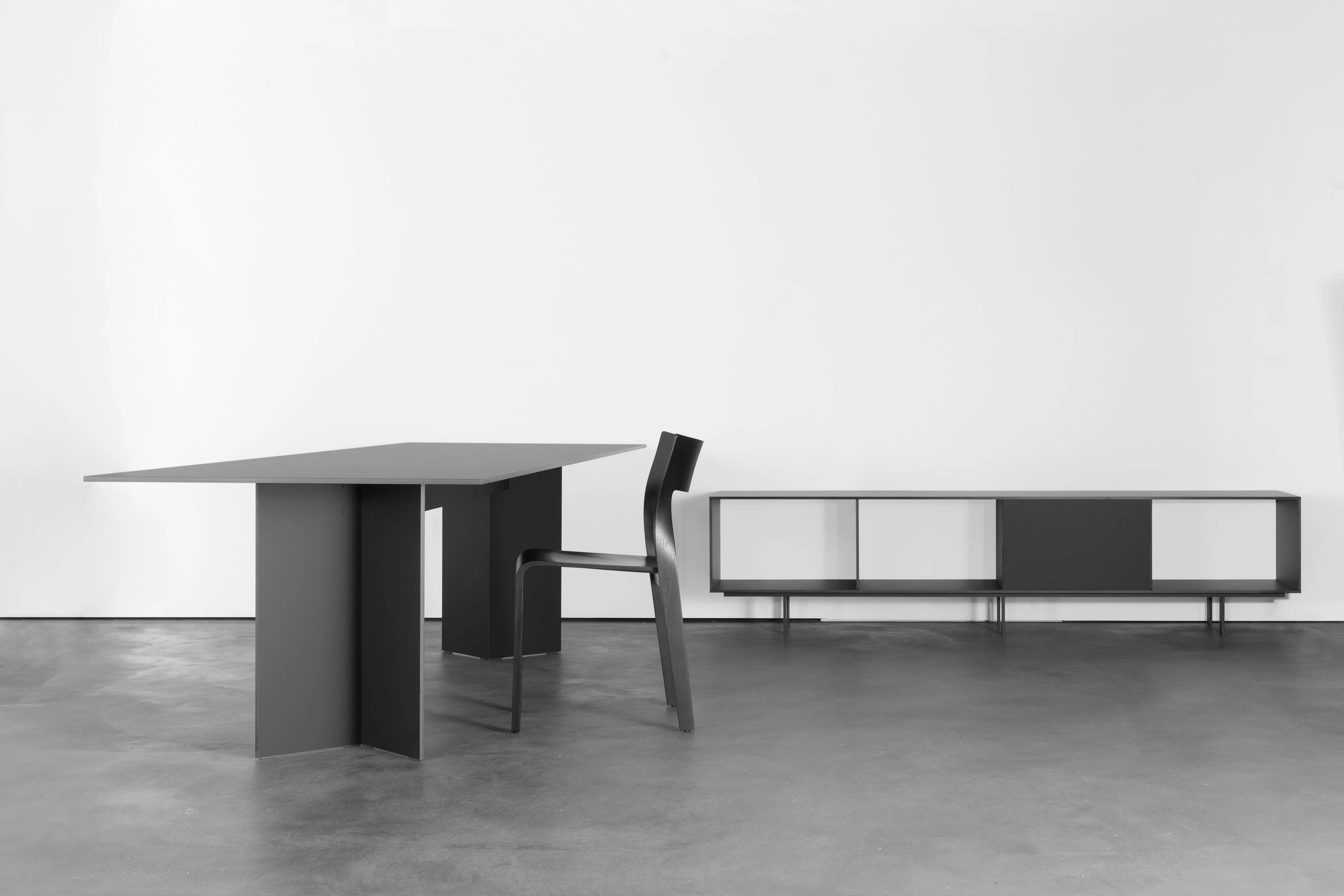 Schwarzer Tisch mit schwarzem Stuhl, dahinter ein langes Sideboard mit weissen und schwarzen Fronten.