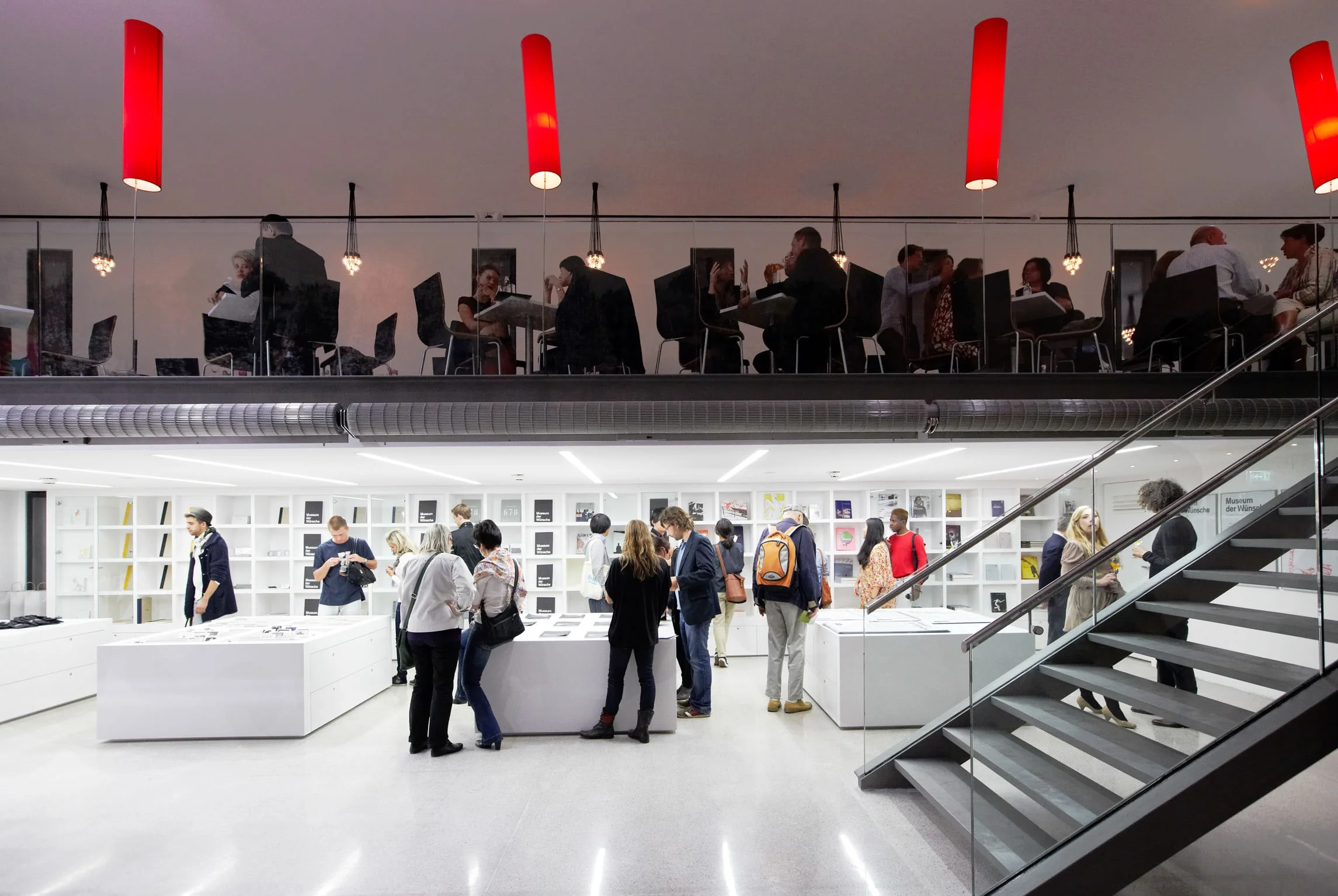 Museumsrestaurant auf einer Galerie mit roten Hängeleuchten, darunter der Shop mit Besuchern.