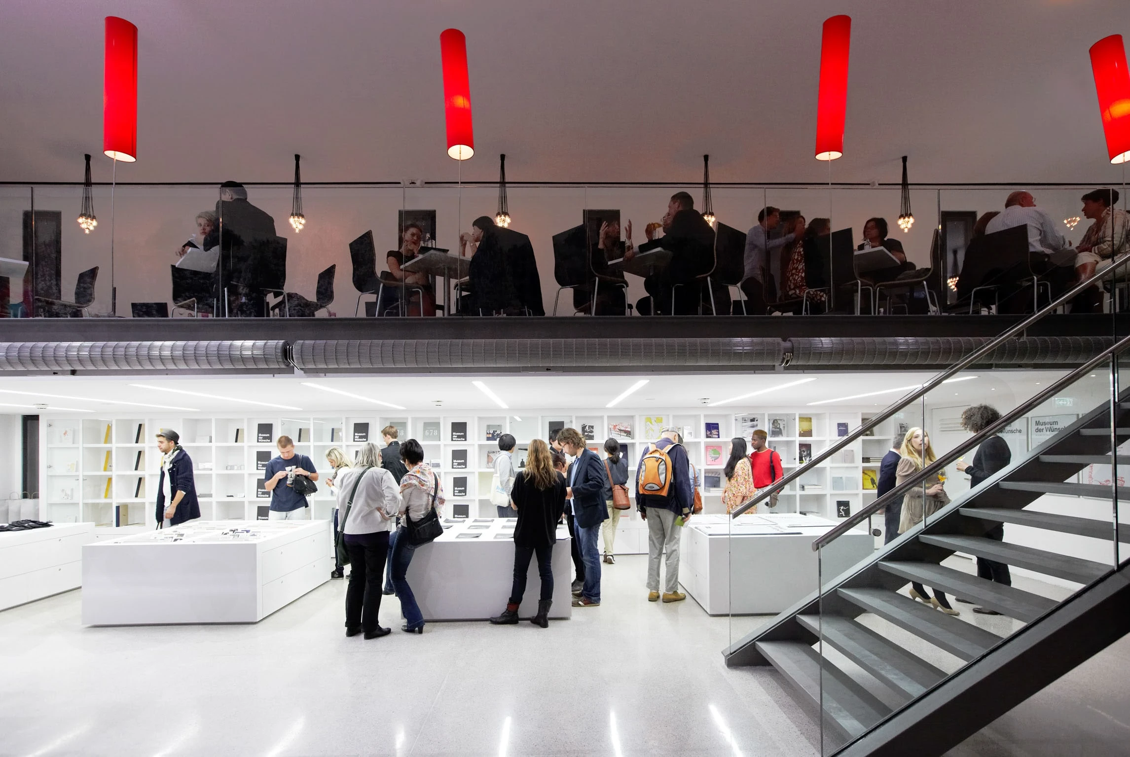 Museumsrestaurant auf einer Galerie mit roten Hängeleuchten, darunter der Shop mit Besuchern.