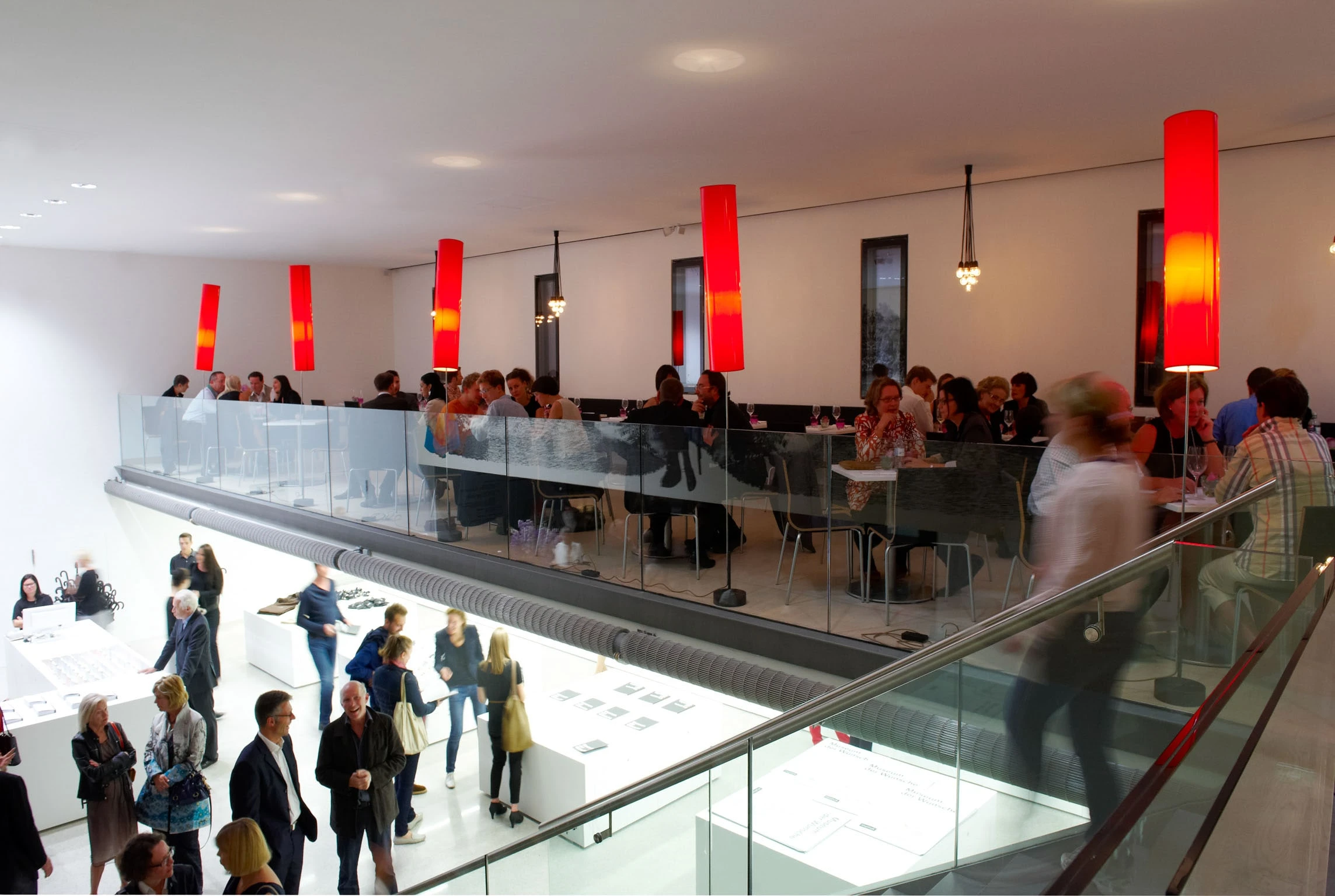 Galerie des Museumsrestaurants mit Gästen hinter einer Glasbrüstung und roten Leuchten.