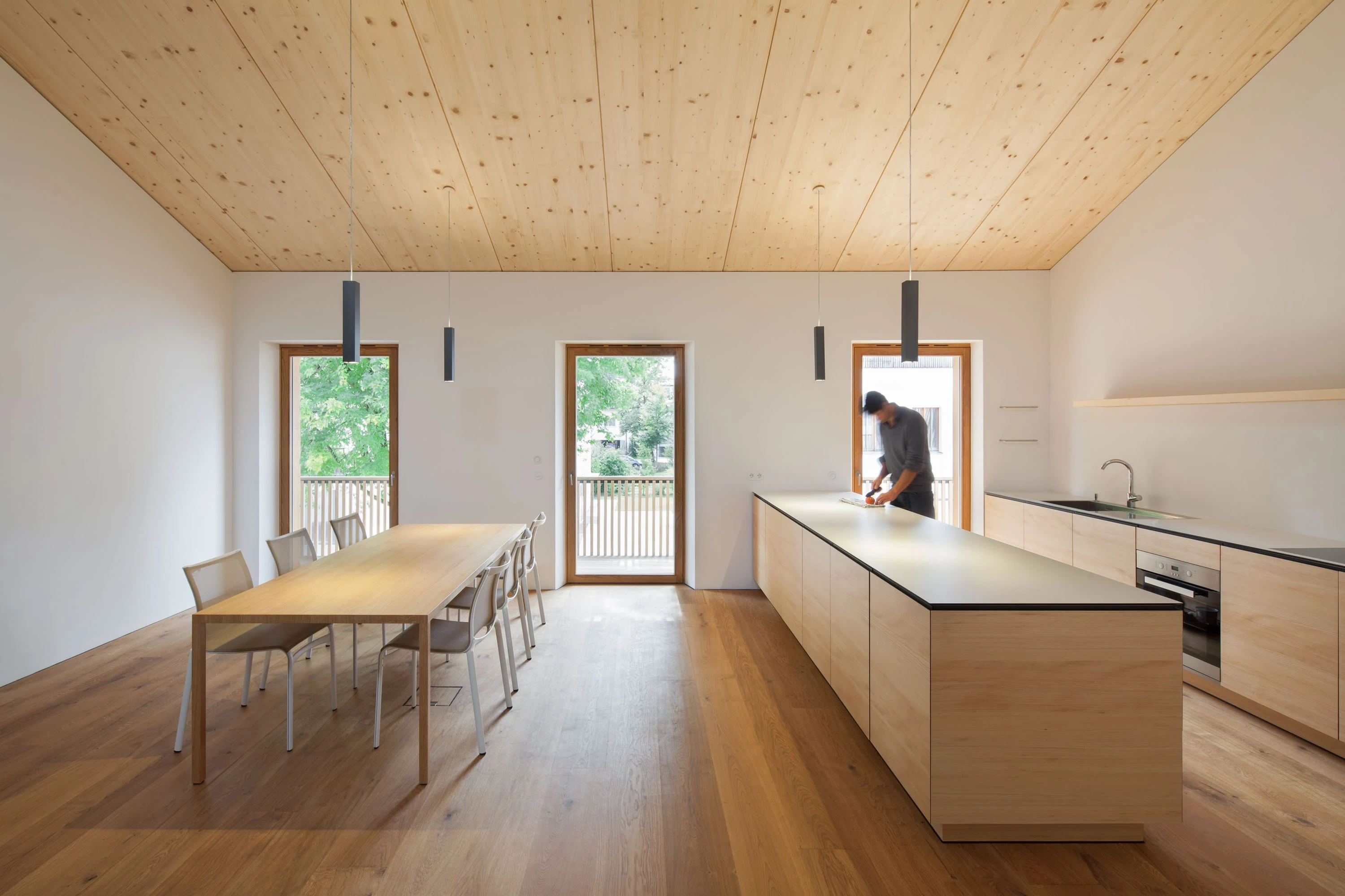 Wohnküche mit Holzdecke, langem Esstisch, Kücheninsel und Fenstertüren.