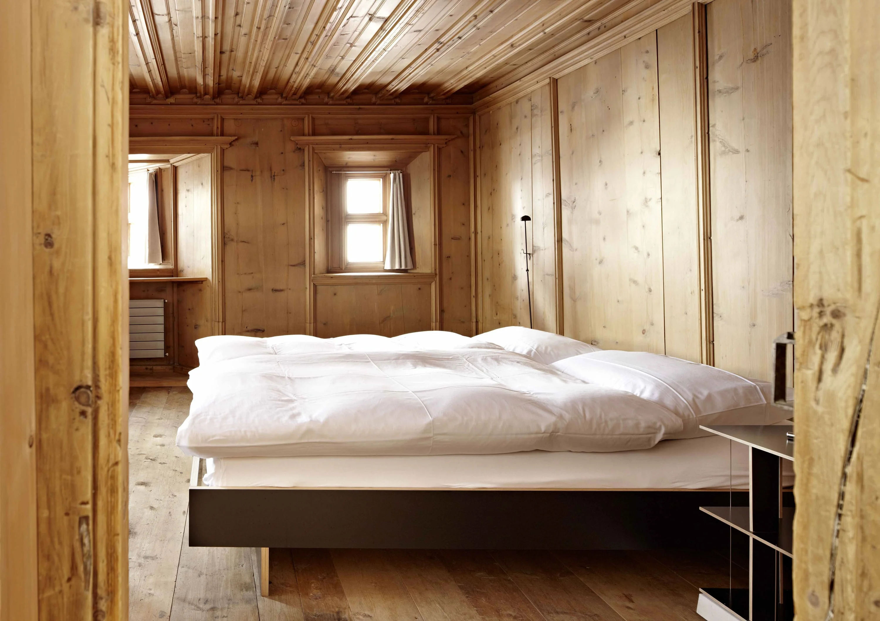 Holzvertäfeltes Schlafzimmer mit breitem Bett und weisser Bettwäsche.