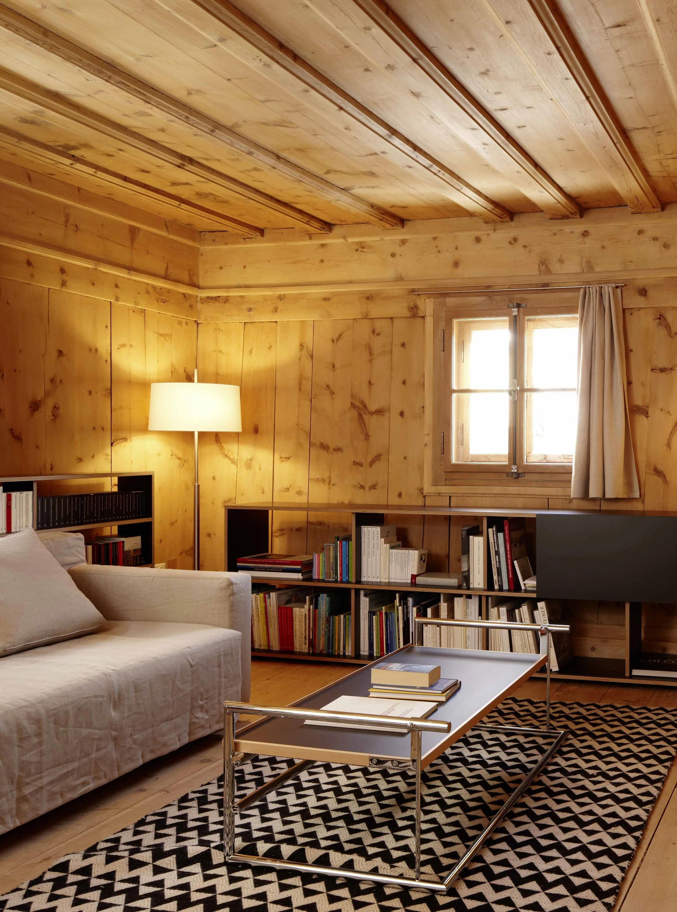 Wohnraum mit Holzbalkendecke, Sofa, Couchtisch und Bücherregal.