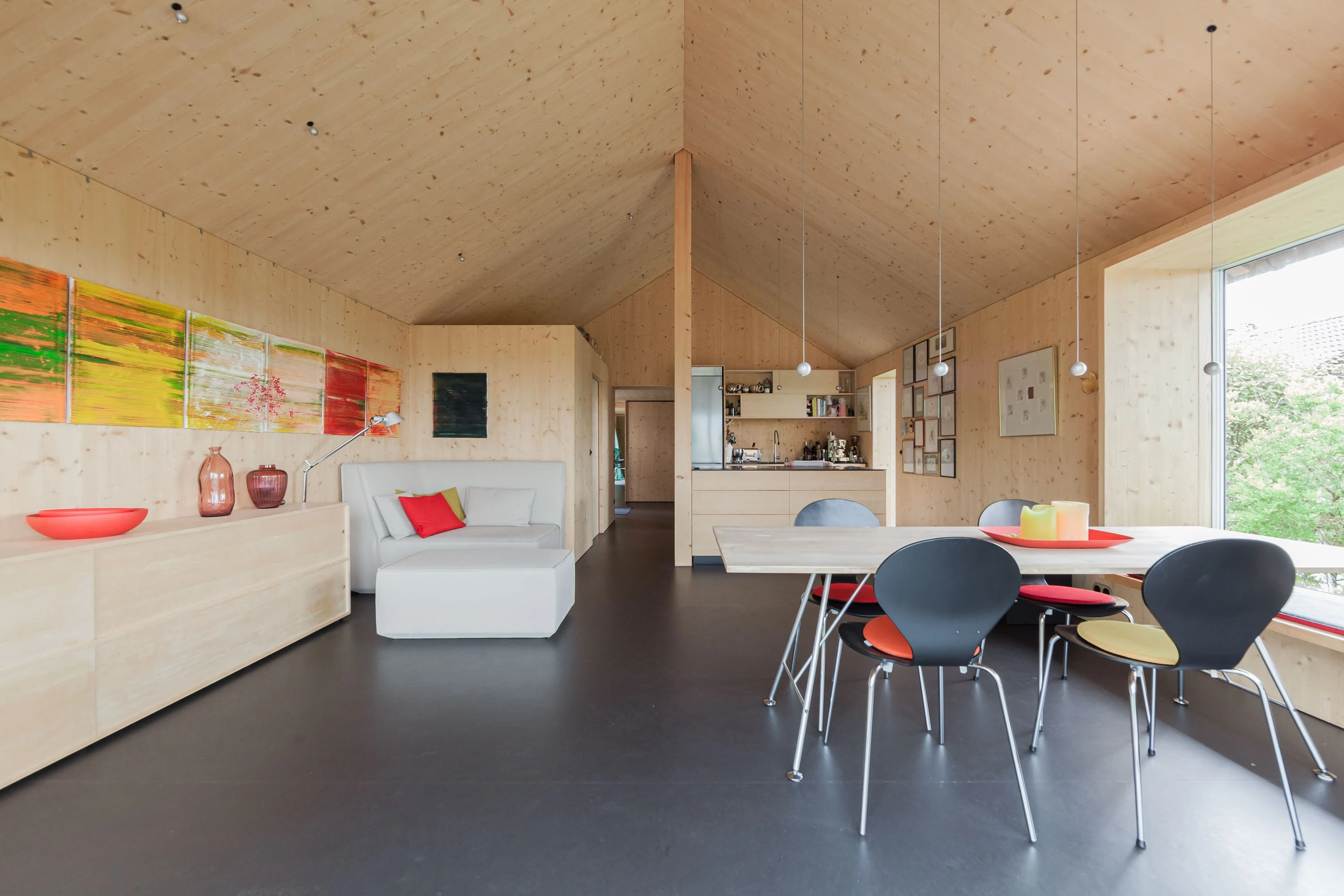 Essbereich mit Holzwänden, Tisch mit farbigen Stühlen und Sideboard unter Gemälden.