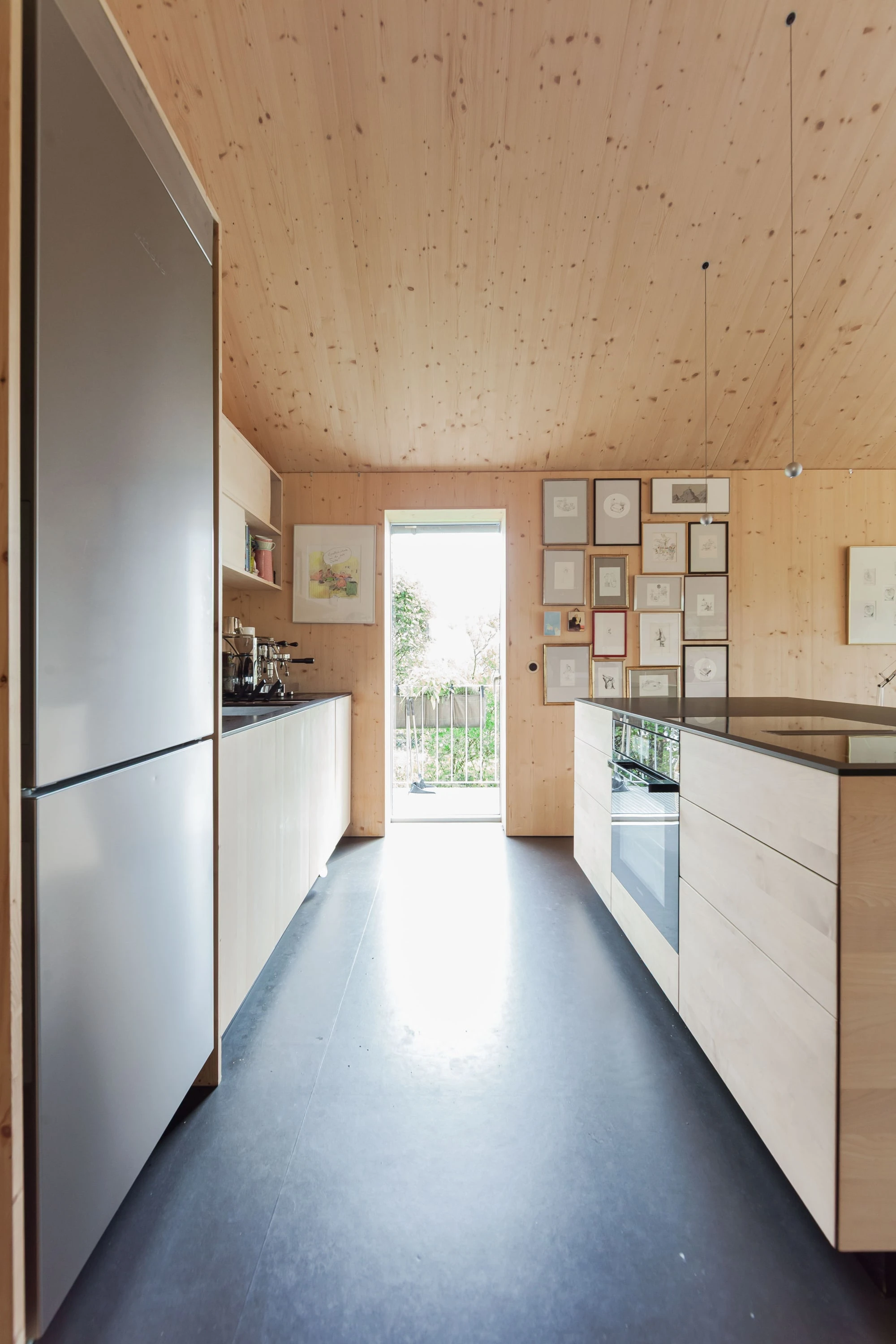 Schmale Küche mit Holzdecke, Hochschrank und Tür nach draussen.