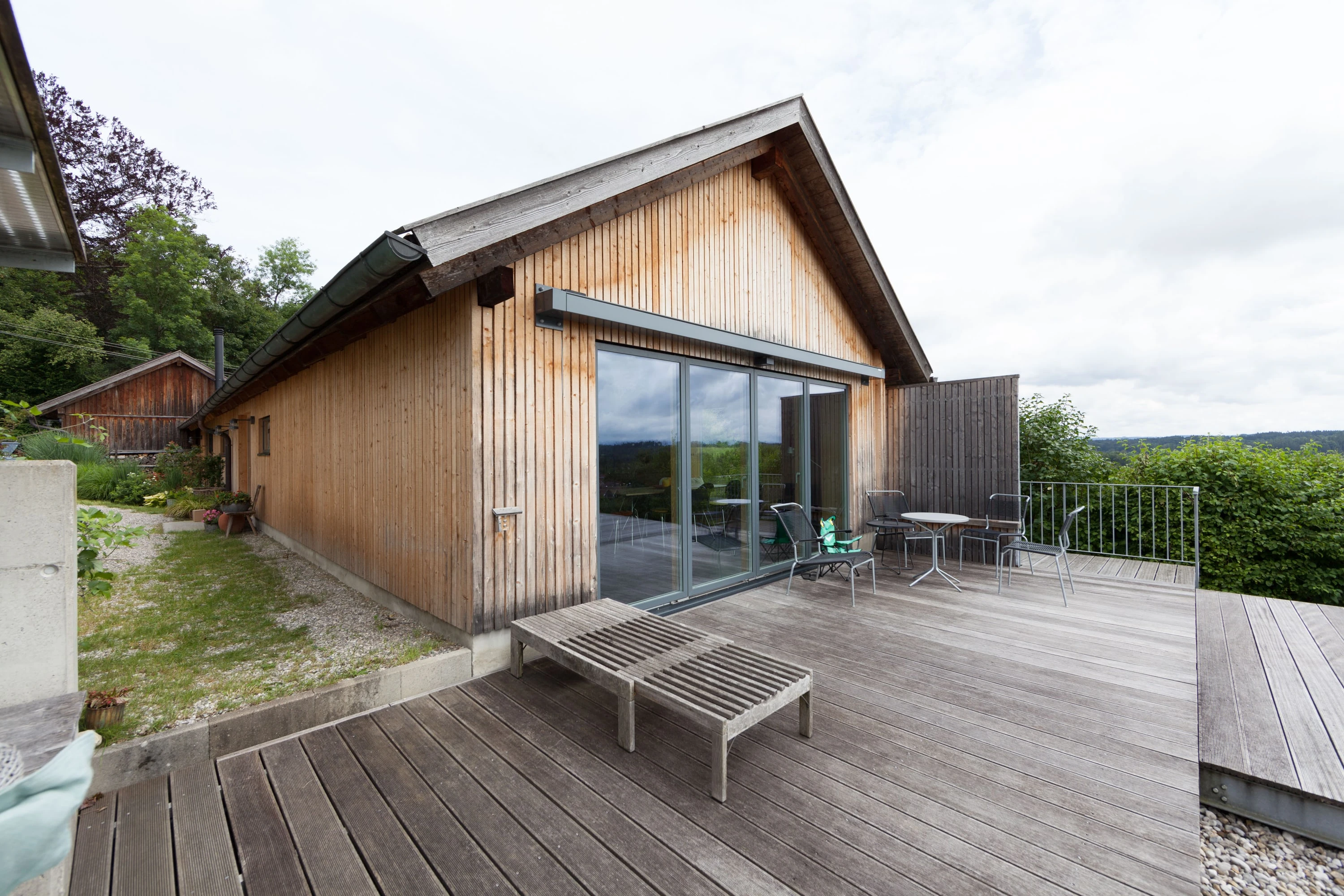 Holzhaus mit grosser Glasfront und Holzterrasse mit Liegen.