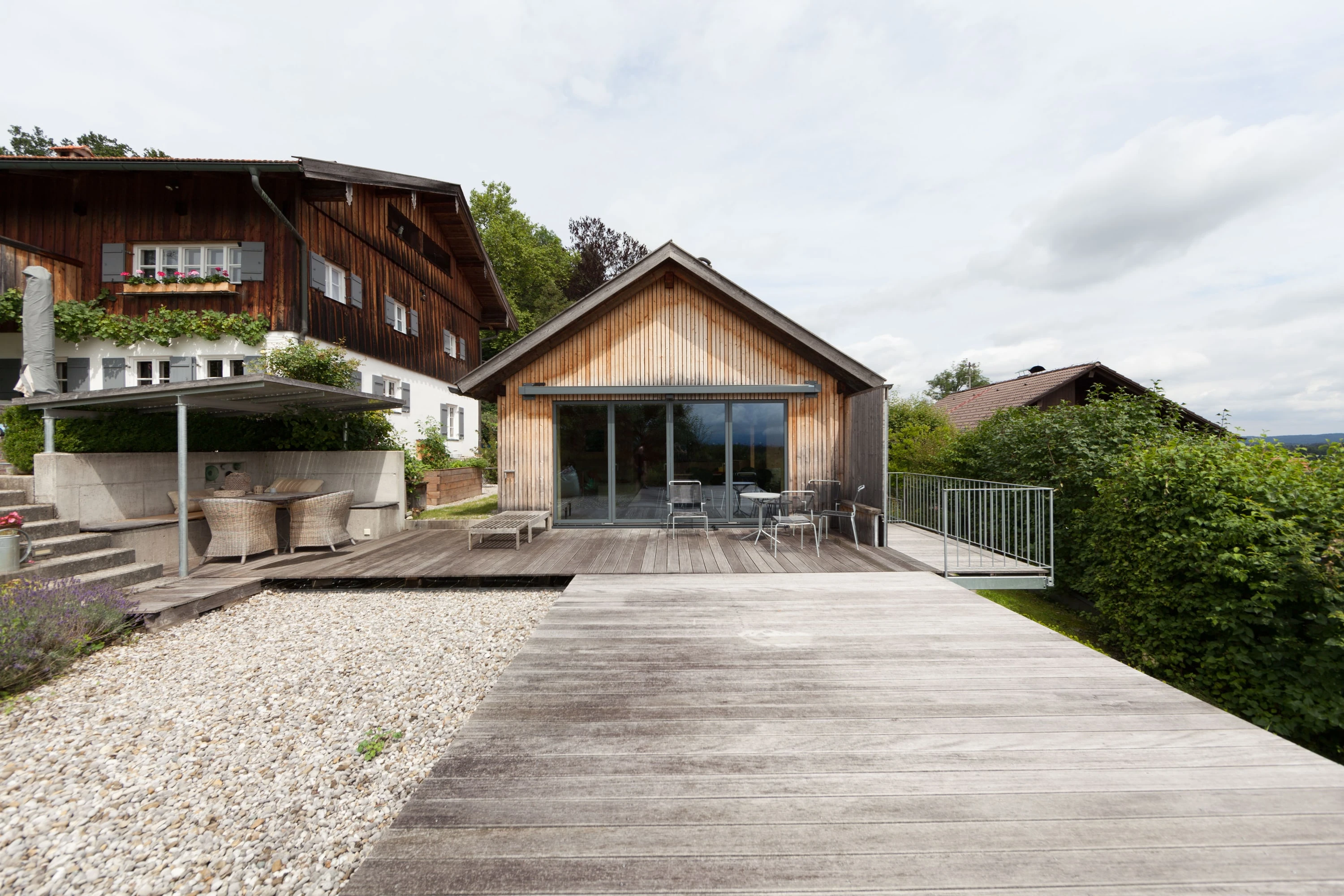 Blick über die Terrasse auf den Holzbau und das benachbarte Bauernhaus.
