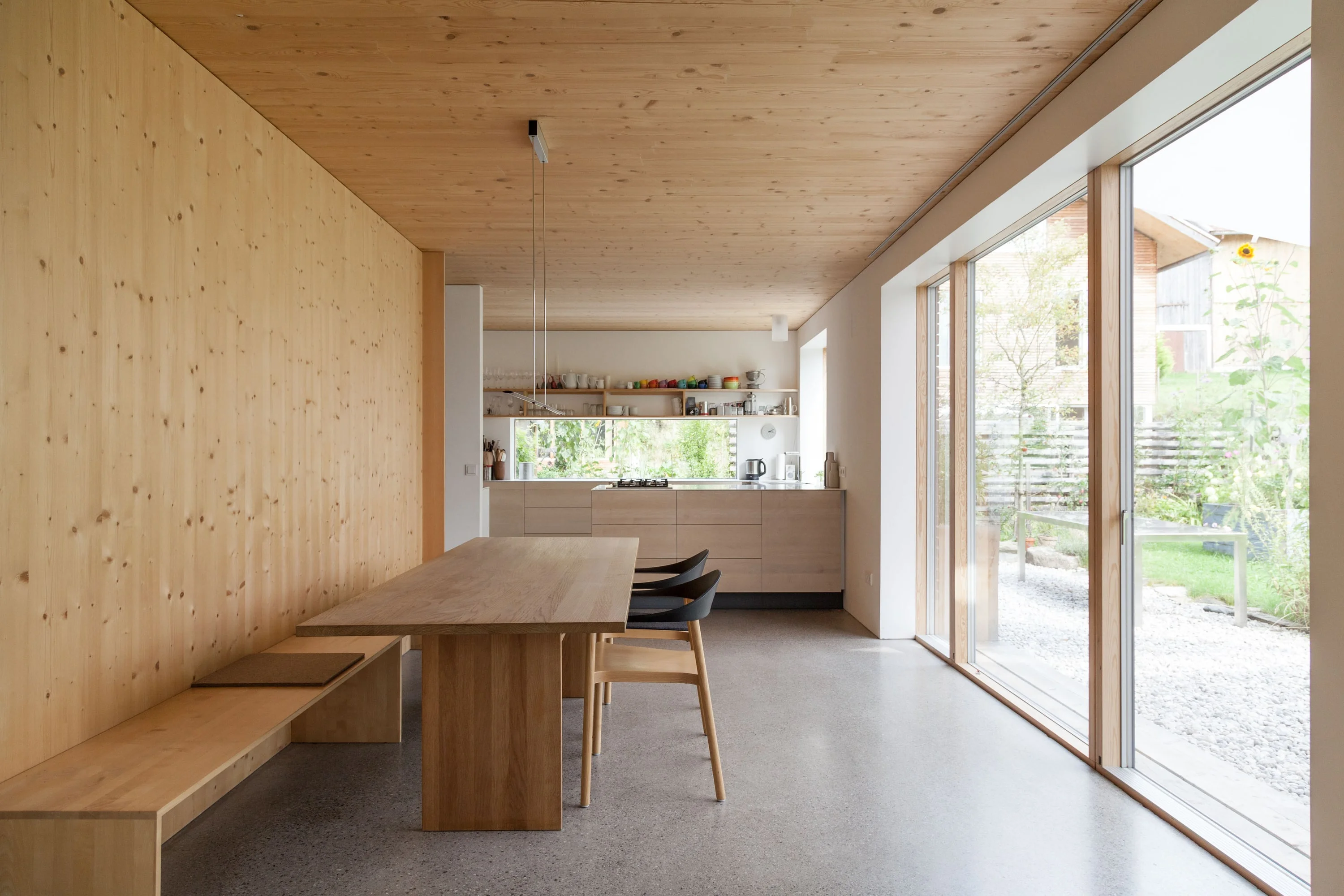 Essraum mit Holzwänden, langem Holztisch mit Bank und grosser Glasfront zum Garten.