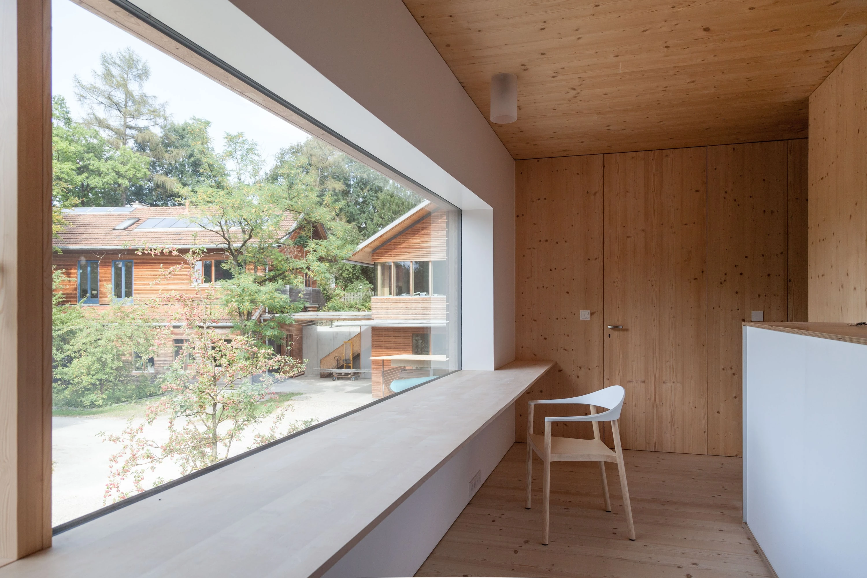 Fensterbank aus Holz mit Stuhl vor einem grossen Fenster mit Blick auf die Nachbarhäuser.