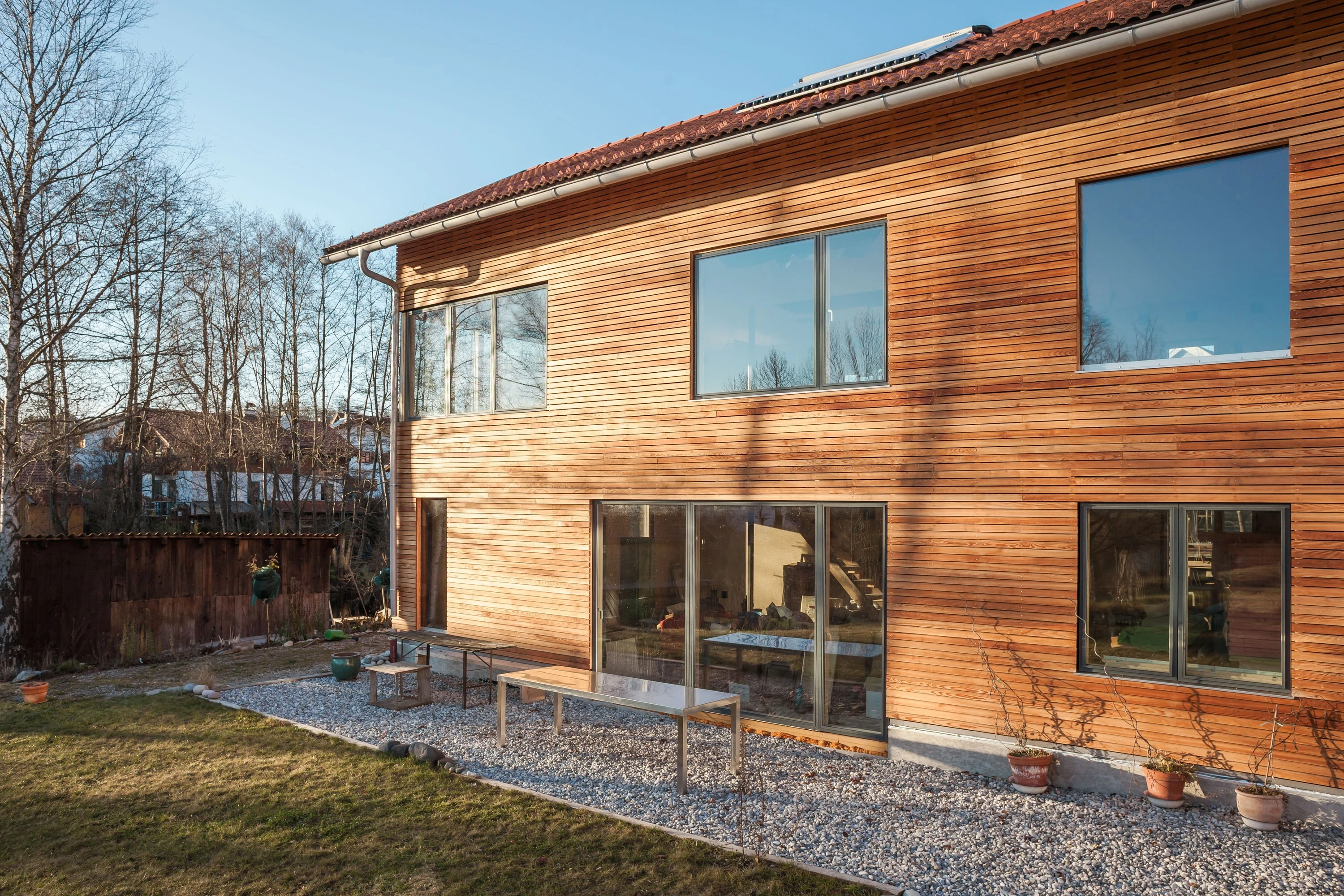 Zweigeschossiges Holzhaus mit Lärchenfassade und grossen Fenstern im Garten.