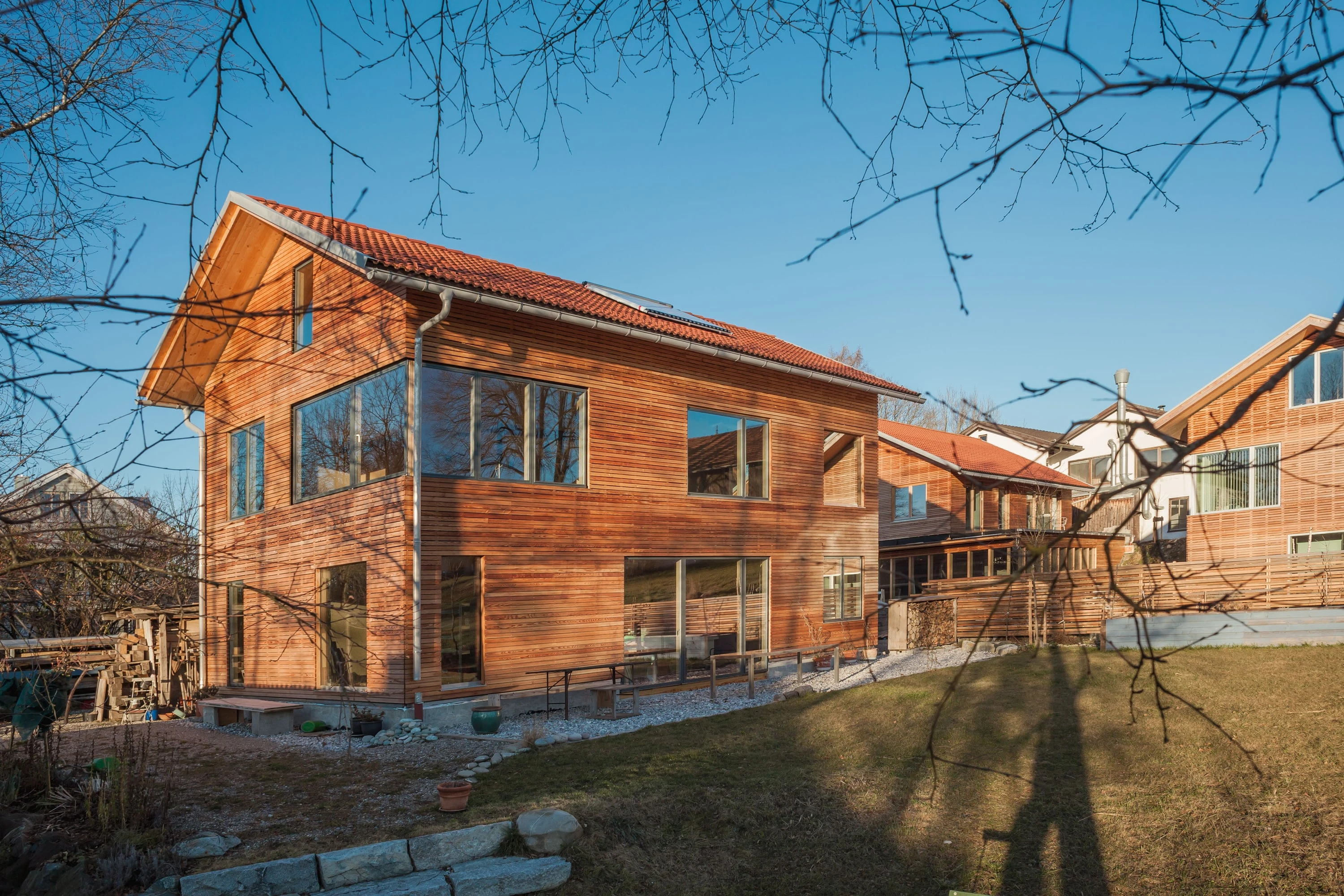 Holzhaus mit Lärchenfassade im Abendlicht, im Vordergrund kahle Äste.