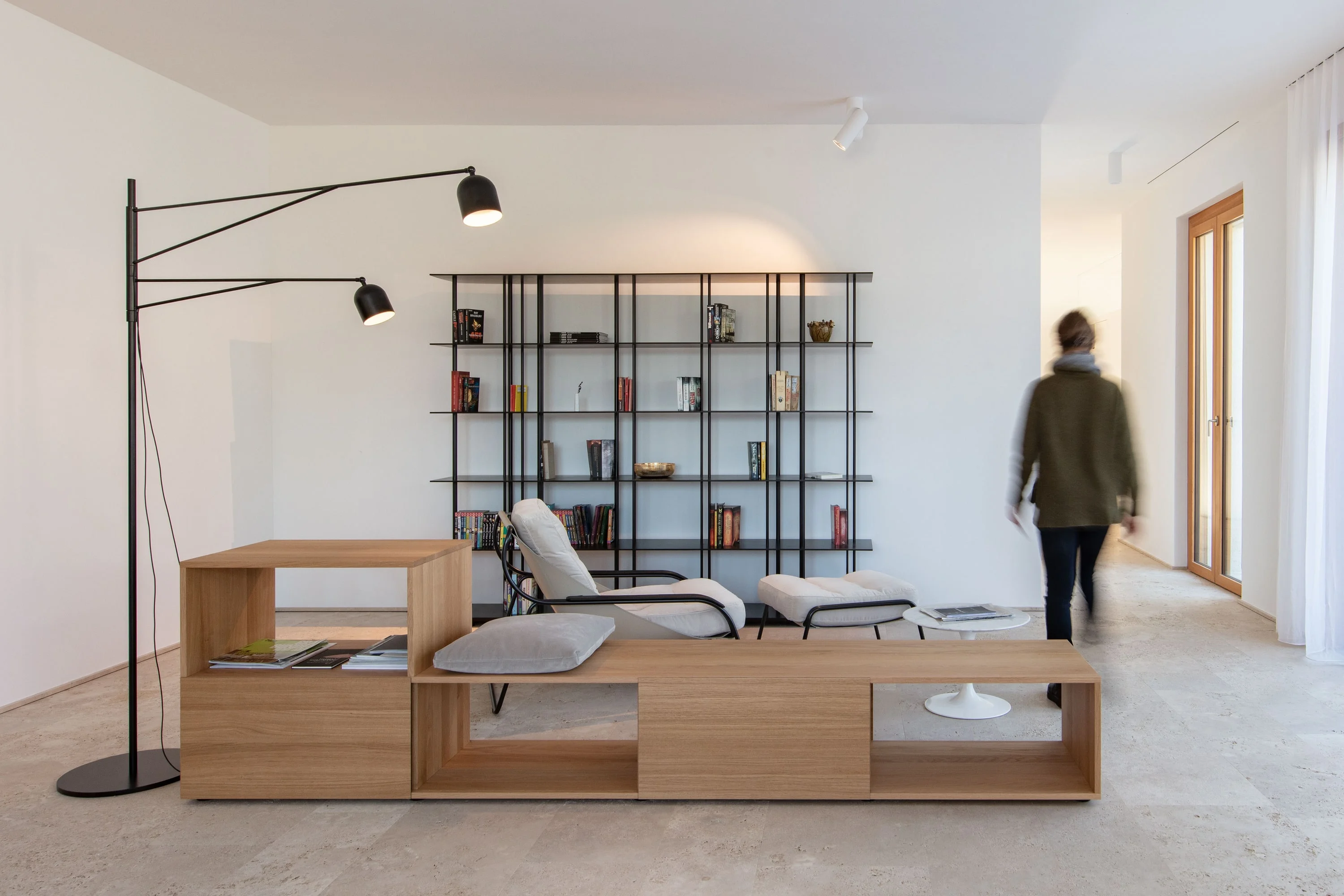 Wohnraum mit Natursteinboden, niedrigem Holzmöbel, Liege und Regal mit Metallstäben.