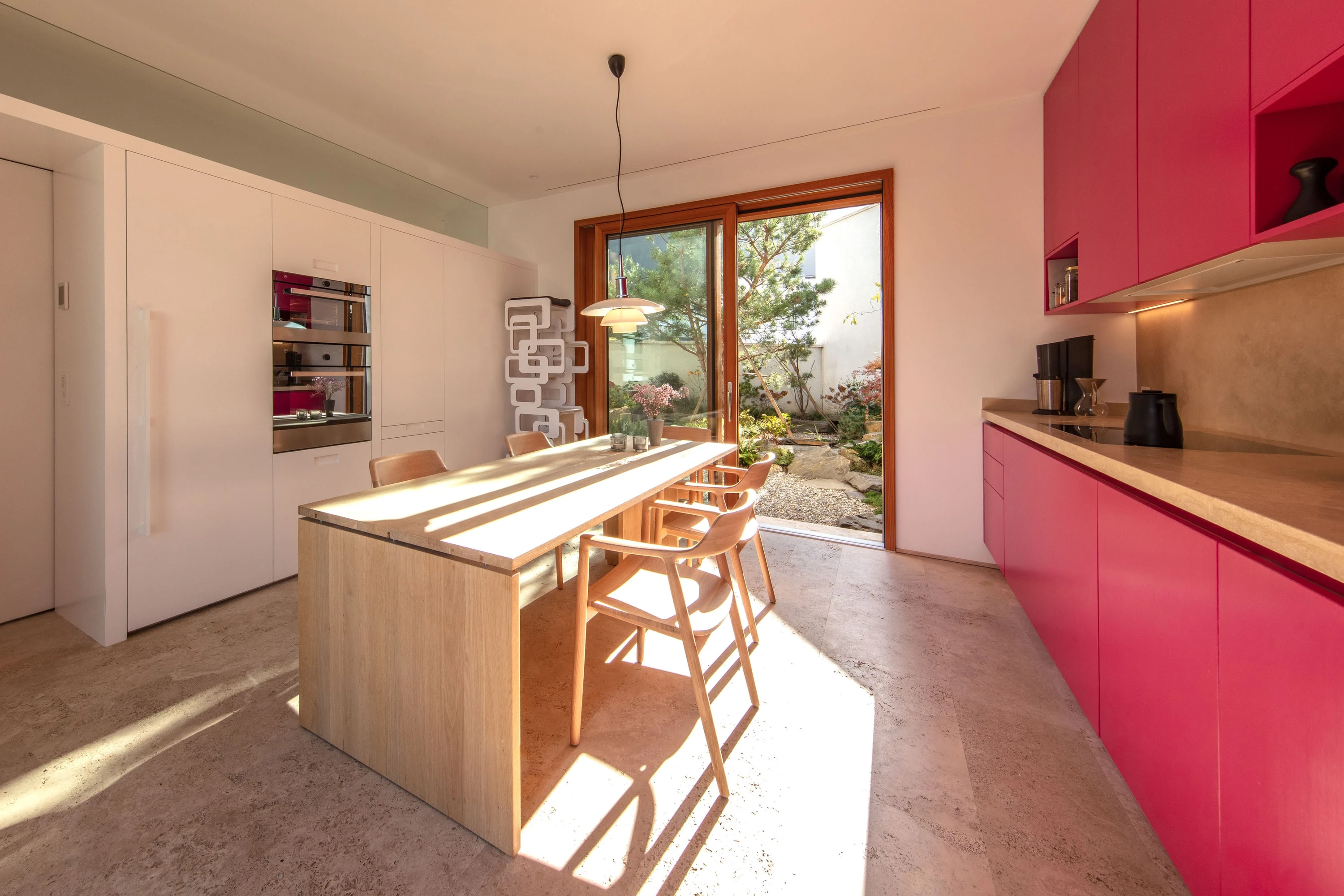 Küche mit roten Fronten und Esstisch aus Holz vor einer geöffneten Glastür.