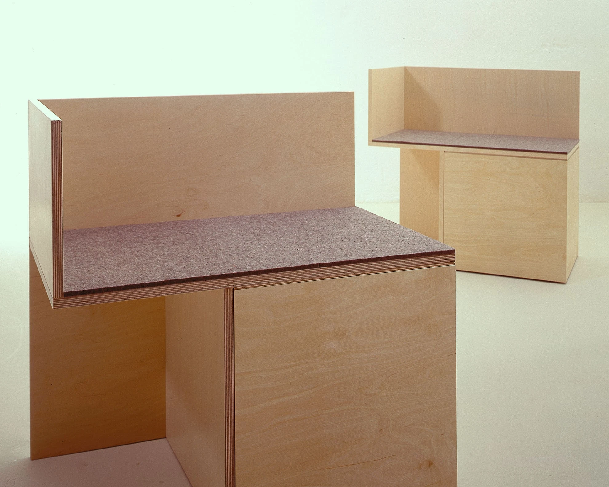Zwei Sitzkuben aus hellem Holz mit hoher Rückwand und Filzsitz.