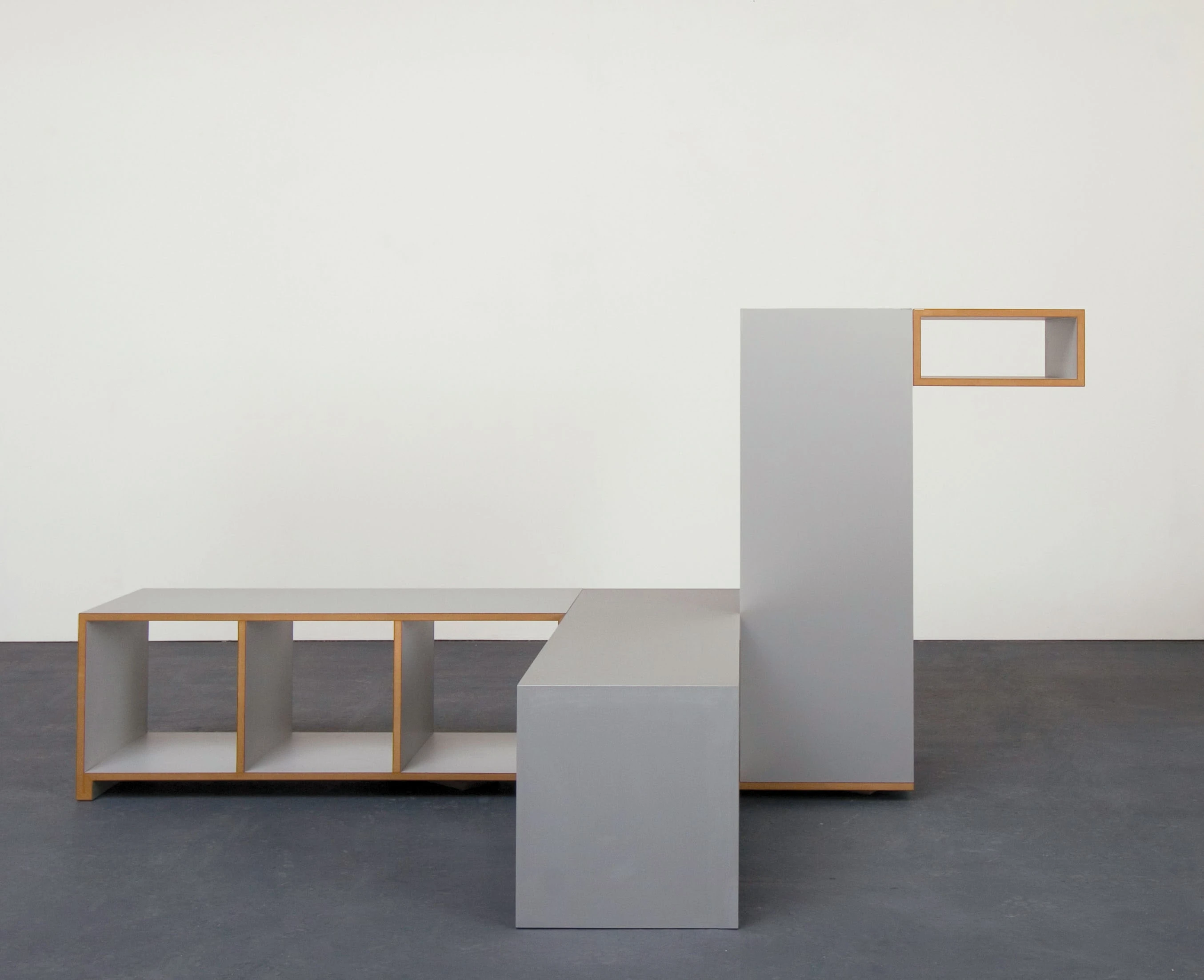 Gray cube used as a seat and surface in front of a low shelf.
