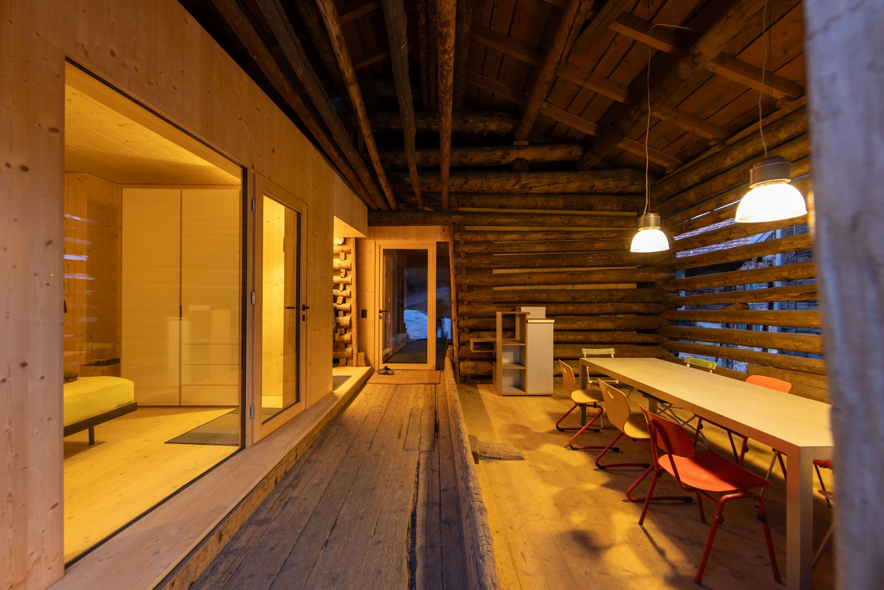 Stallraum aus Rundholz mit eingebautem, beleuchtetem Holzkubus und langem Tisch.
