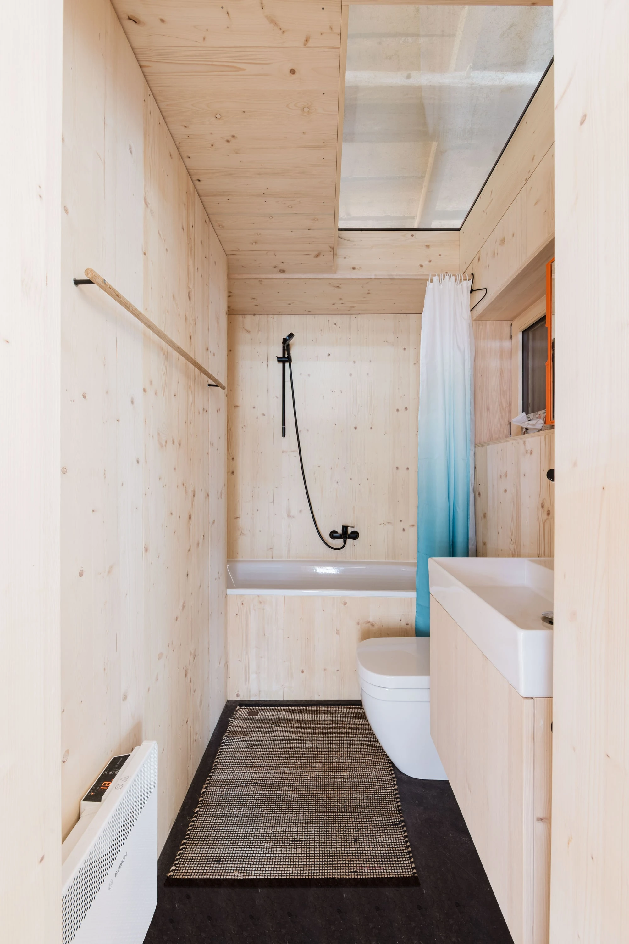 Schmales Bad aus Holz mit Badewanne, Dusche und Oberlicht.