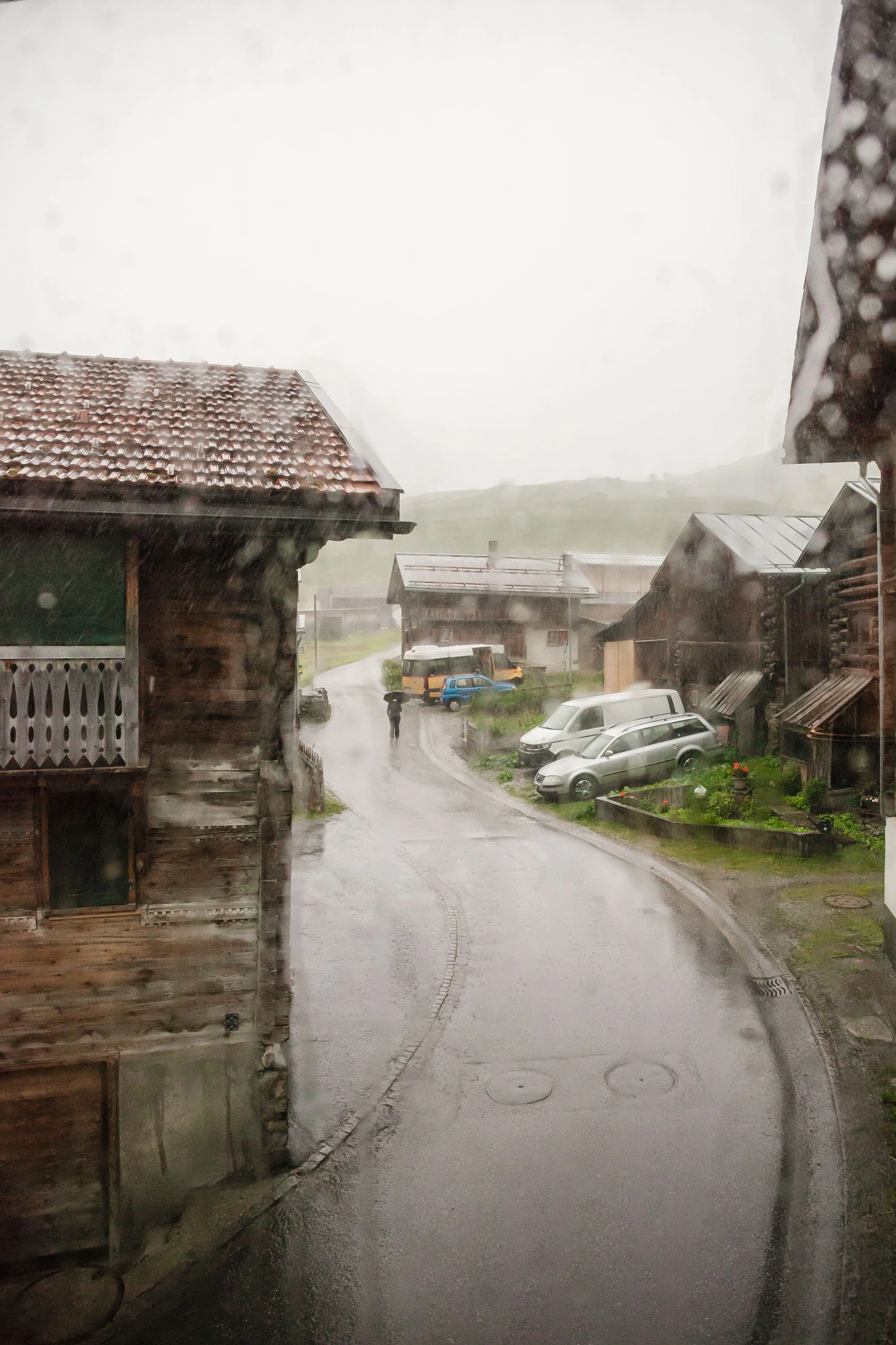 Dorfstrasse in Vrin im Regen zwischen alten Holzhäusern.